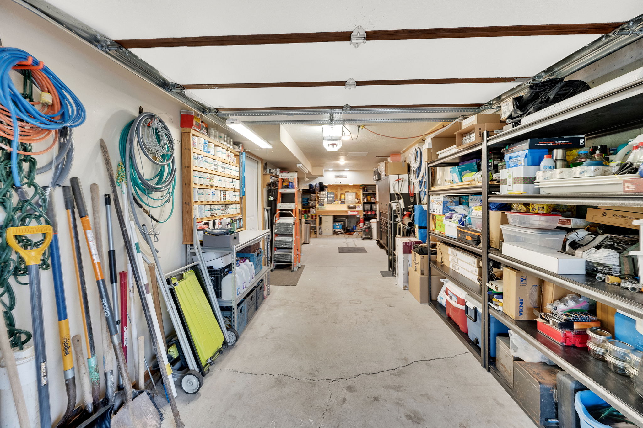 Spacious garage featuring concrete flooring, track lighting, exposed ceiling beams, and ample wall-mounted storage solutions