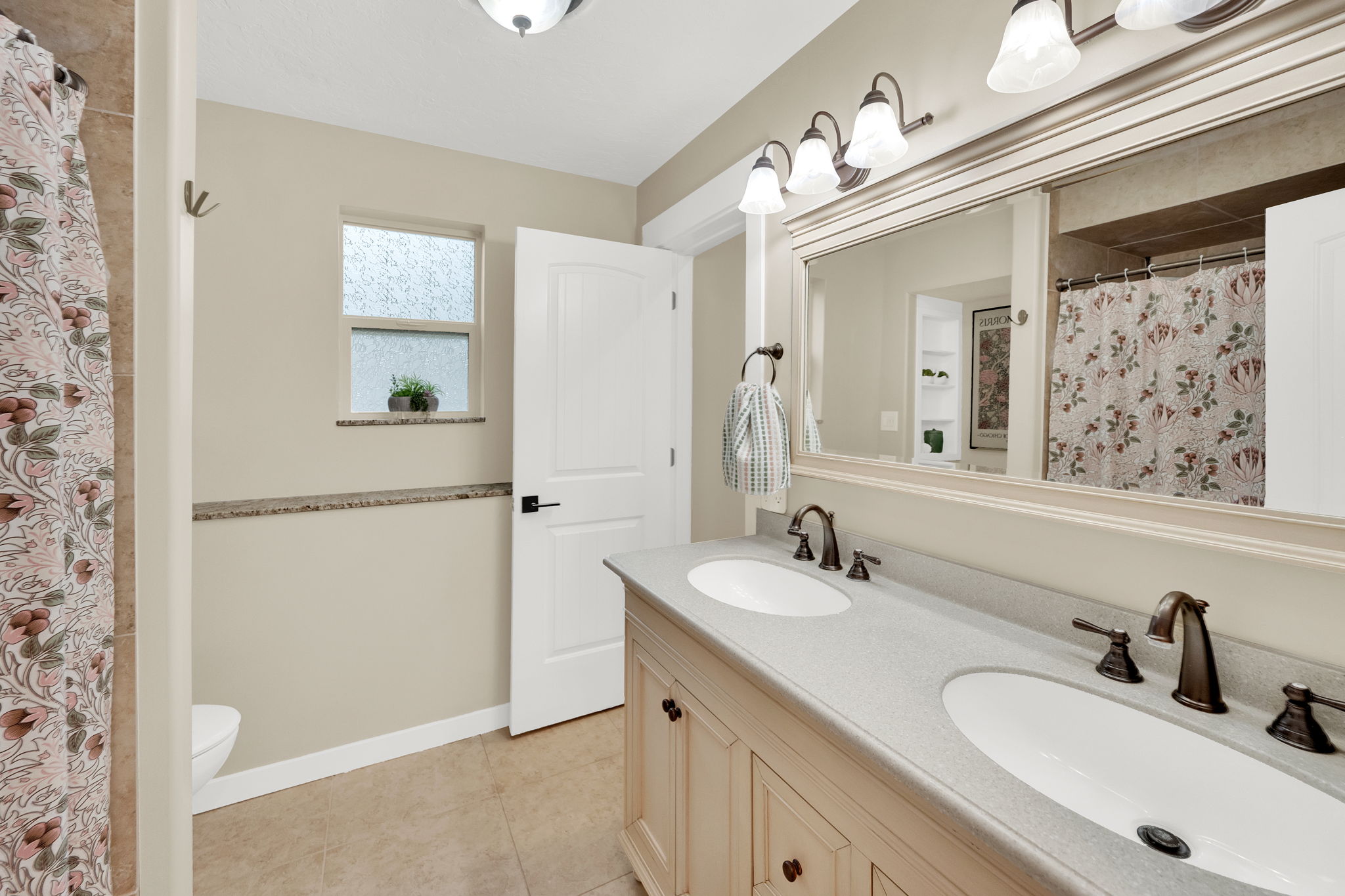 Dual vanity with integrated sinks, brushed bronze fixtures, and a large framed mirror with overhead lighting