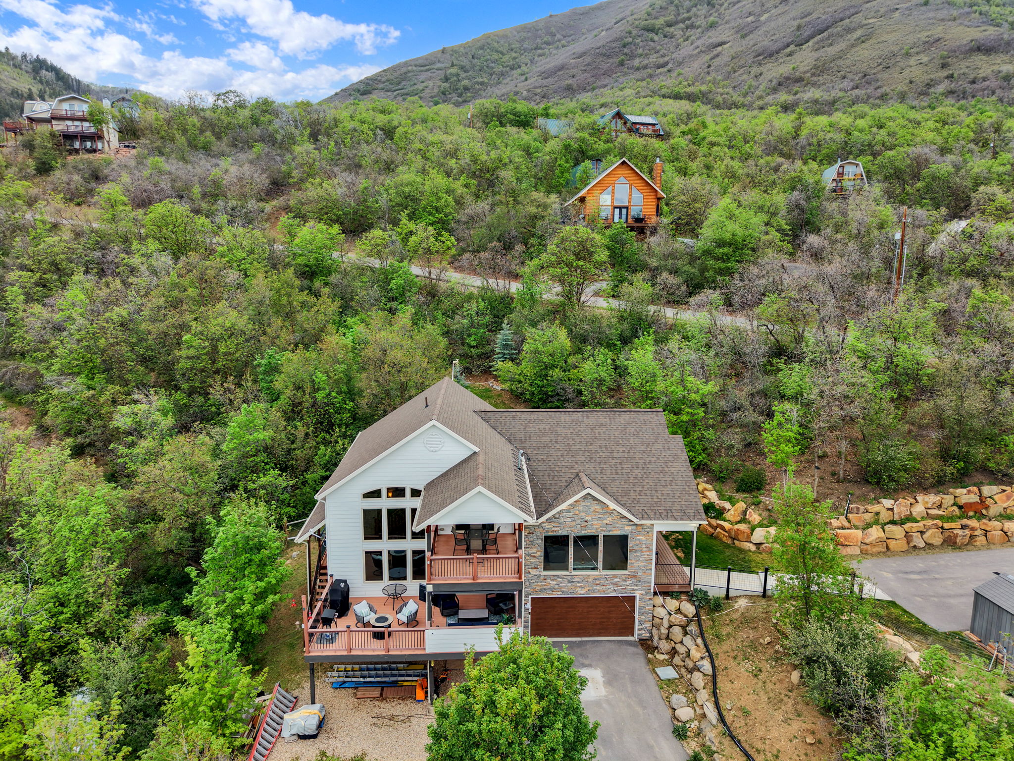 Multi-level residence featuring a stone and siding exterior, expansive terraced decking, and a two-car garage