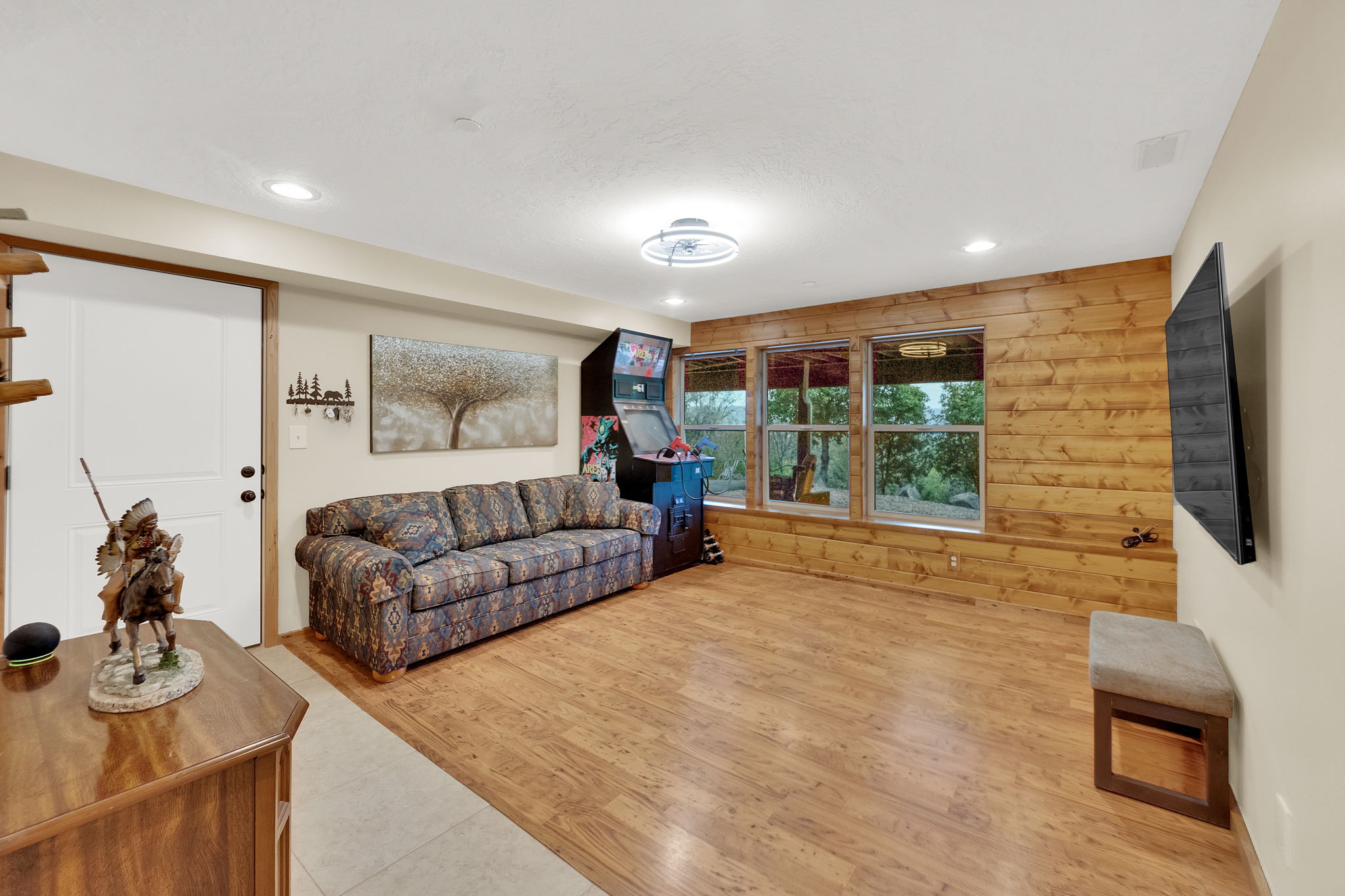 Spacious room featuring wood-finish flooring, a full wall of natural wood paneling, three large windows, recessed lighting, and a white interior door