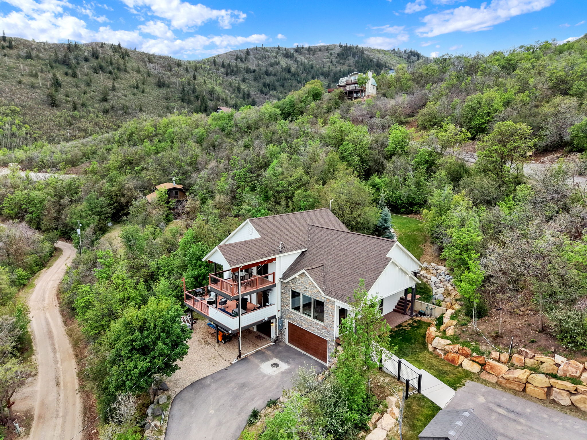 Multi-level home featuring two expansive balconies, a two-car garage with a wood-finish door, stone veneer detailing, and a paved driveway