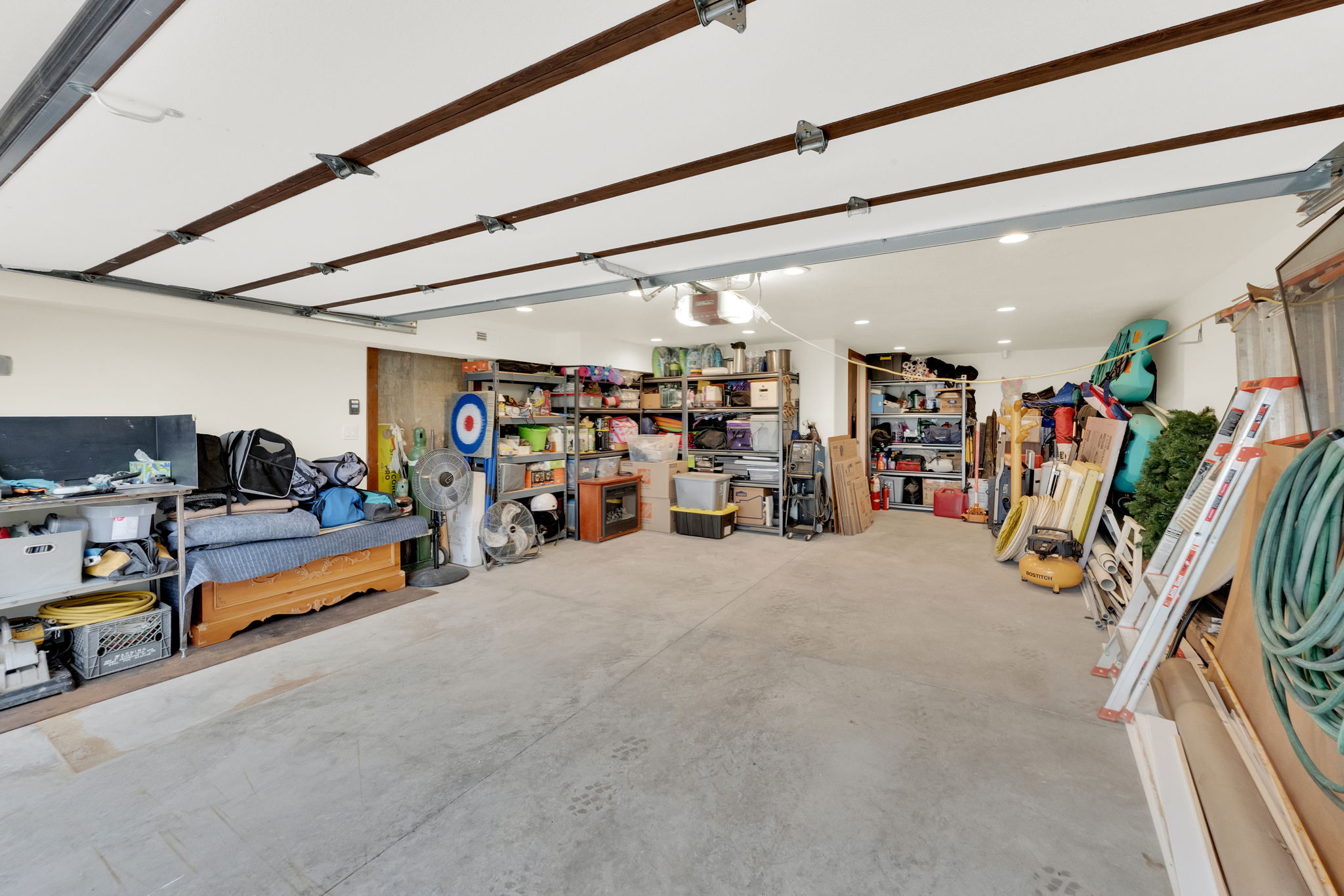 Spacious garage featuring a concrete floor, white walls, exposed ceiling beams, recessed lighting, and shelving for organized storage