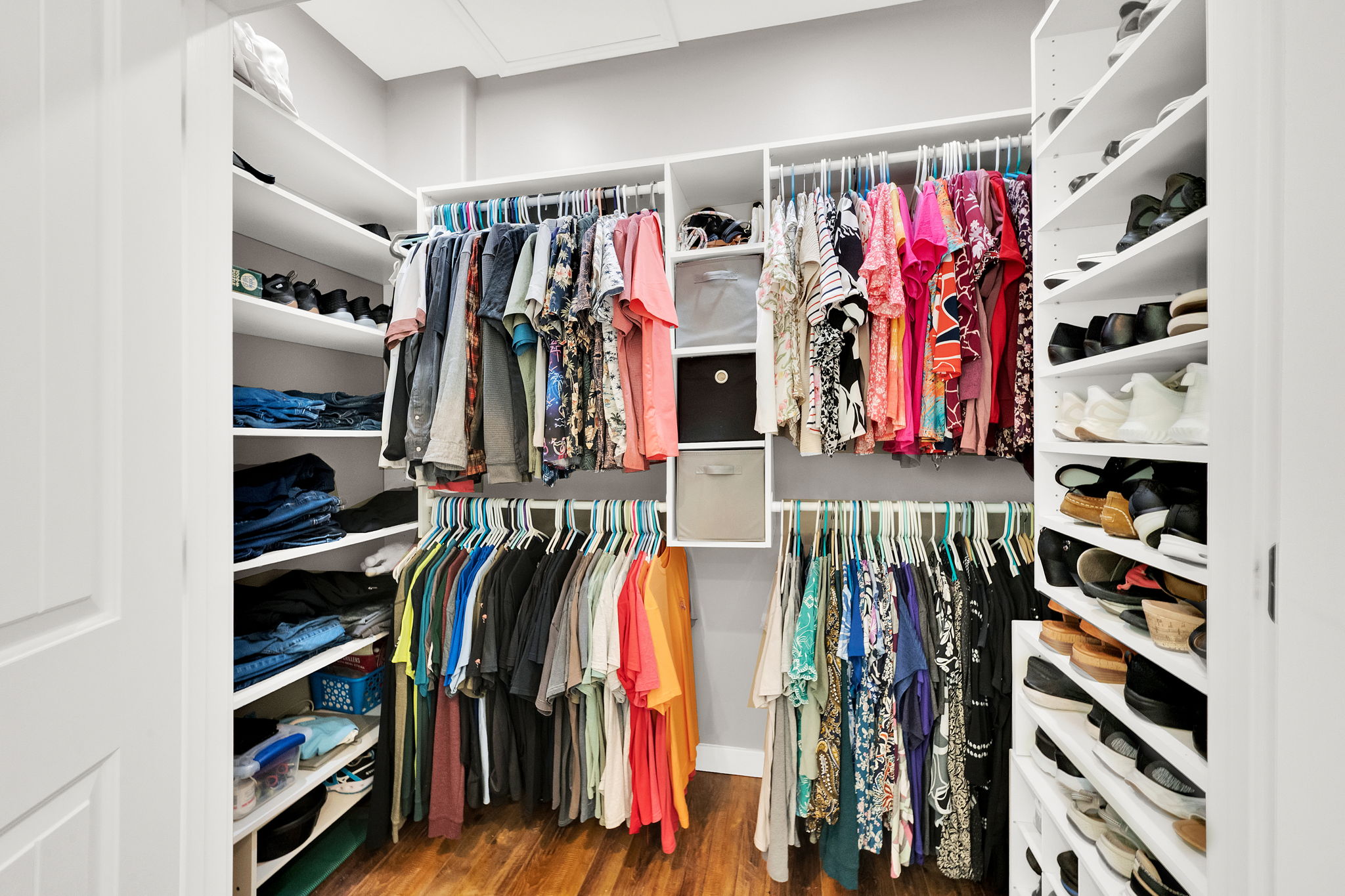 Custom closet system featuring multiple hanging rods, integrated shelving, vertical shoe storage, and wood-finish flooring