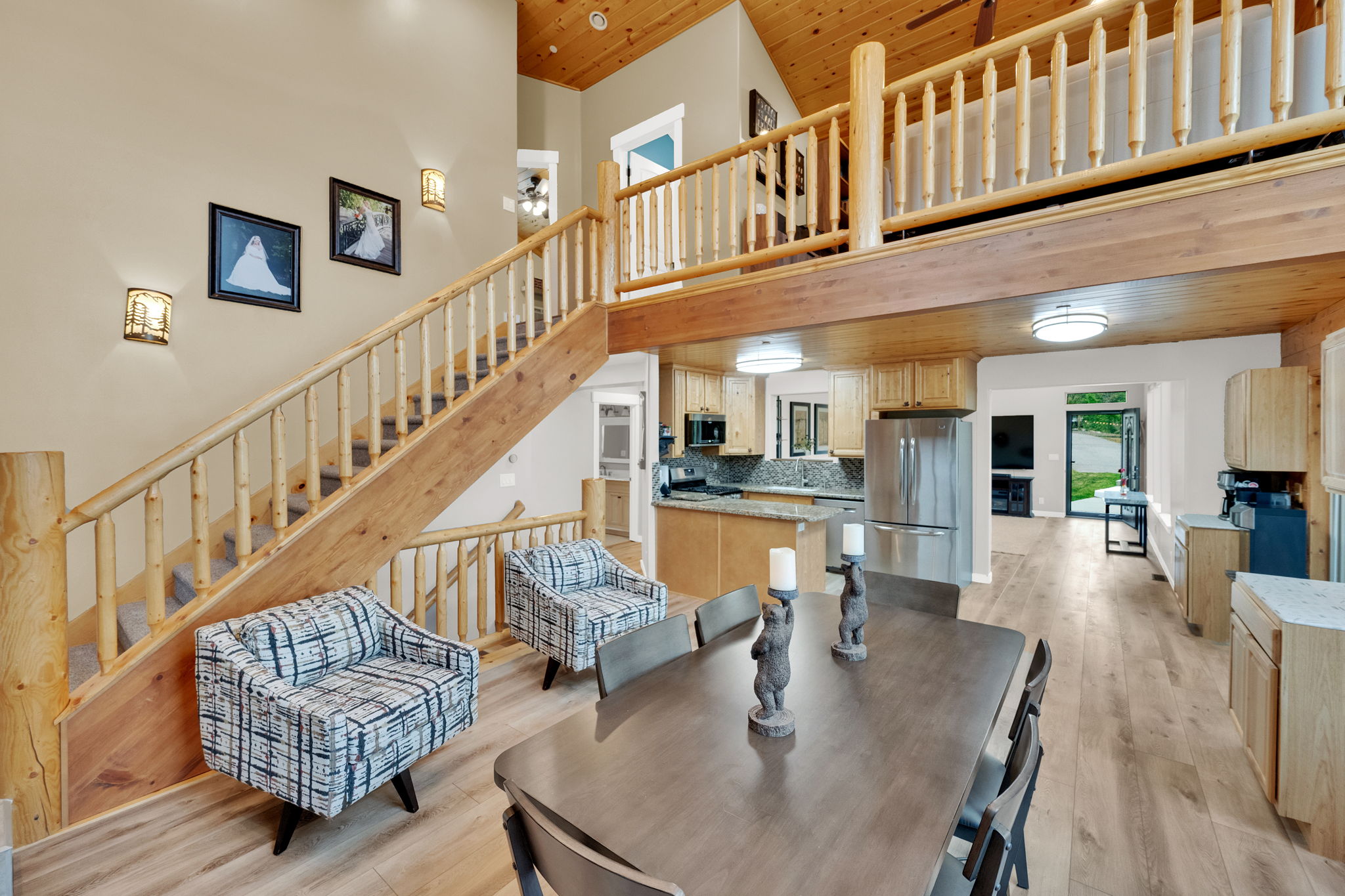 Vaulted ceiling with wood-finish planks, open-concept floor plan, wood-finish flooring, staircase with natural wood railings, and a kitchen featuring stainless steel appliances