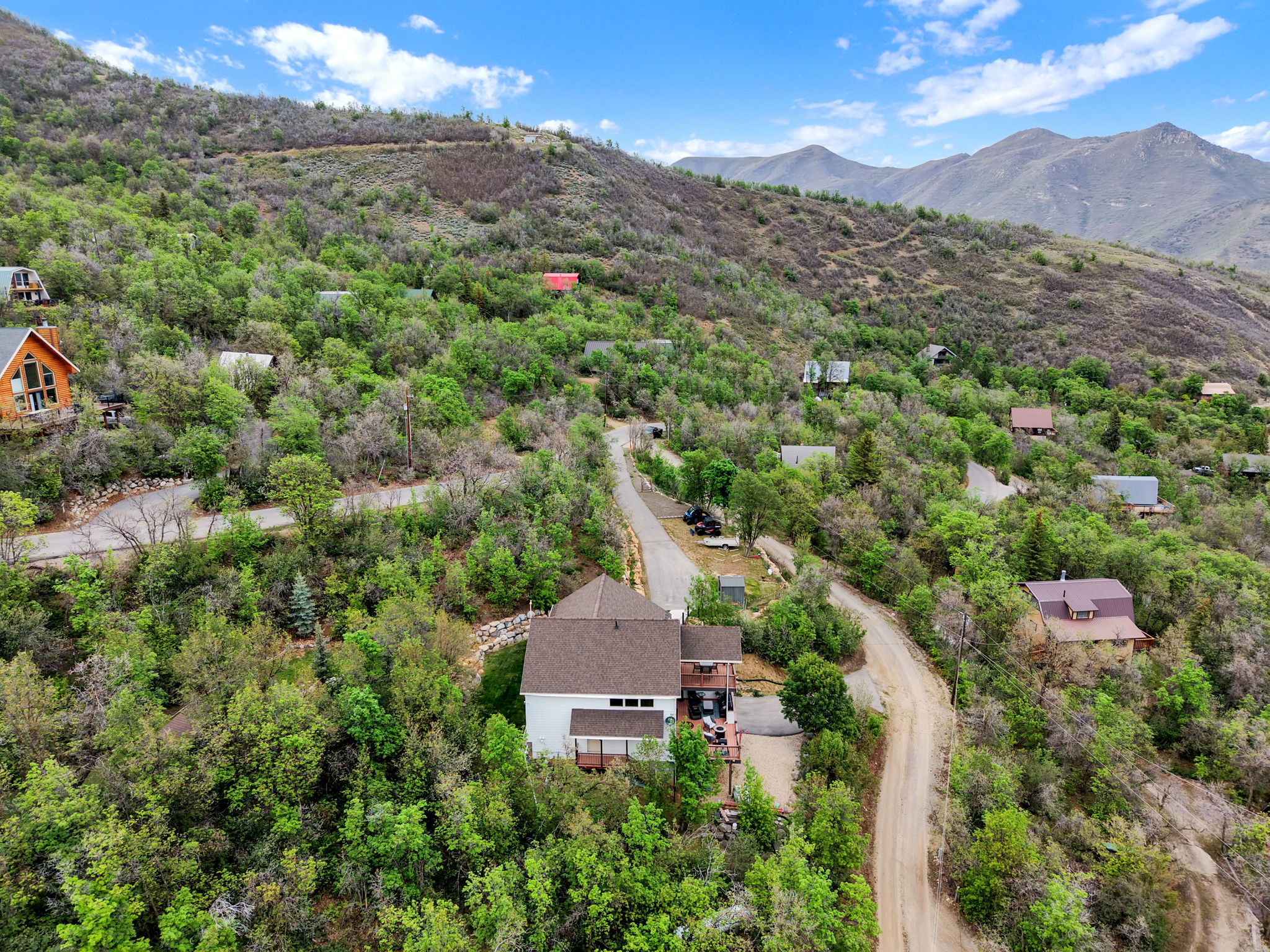 Hillside property featuring a multi-story residence with a brown shingle roof, surrounded by mature trees and natural landscaping
