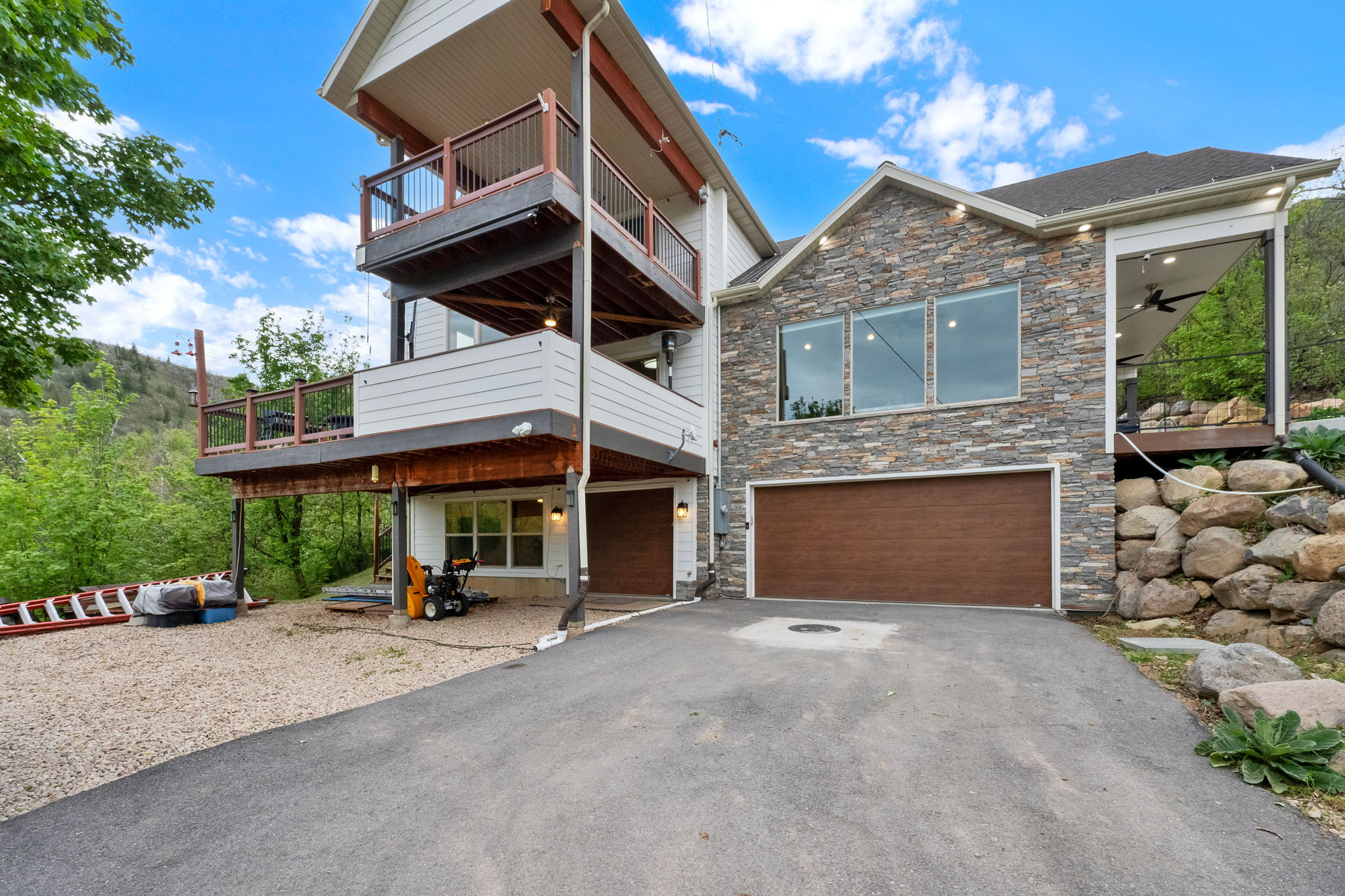 Multi-level residence featuring stacked balconies with dark wood railings, a stone facade, and a wood-finish garage door