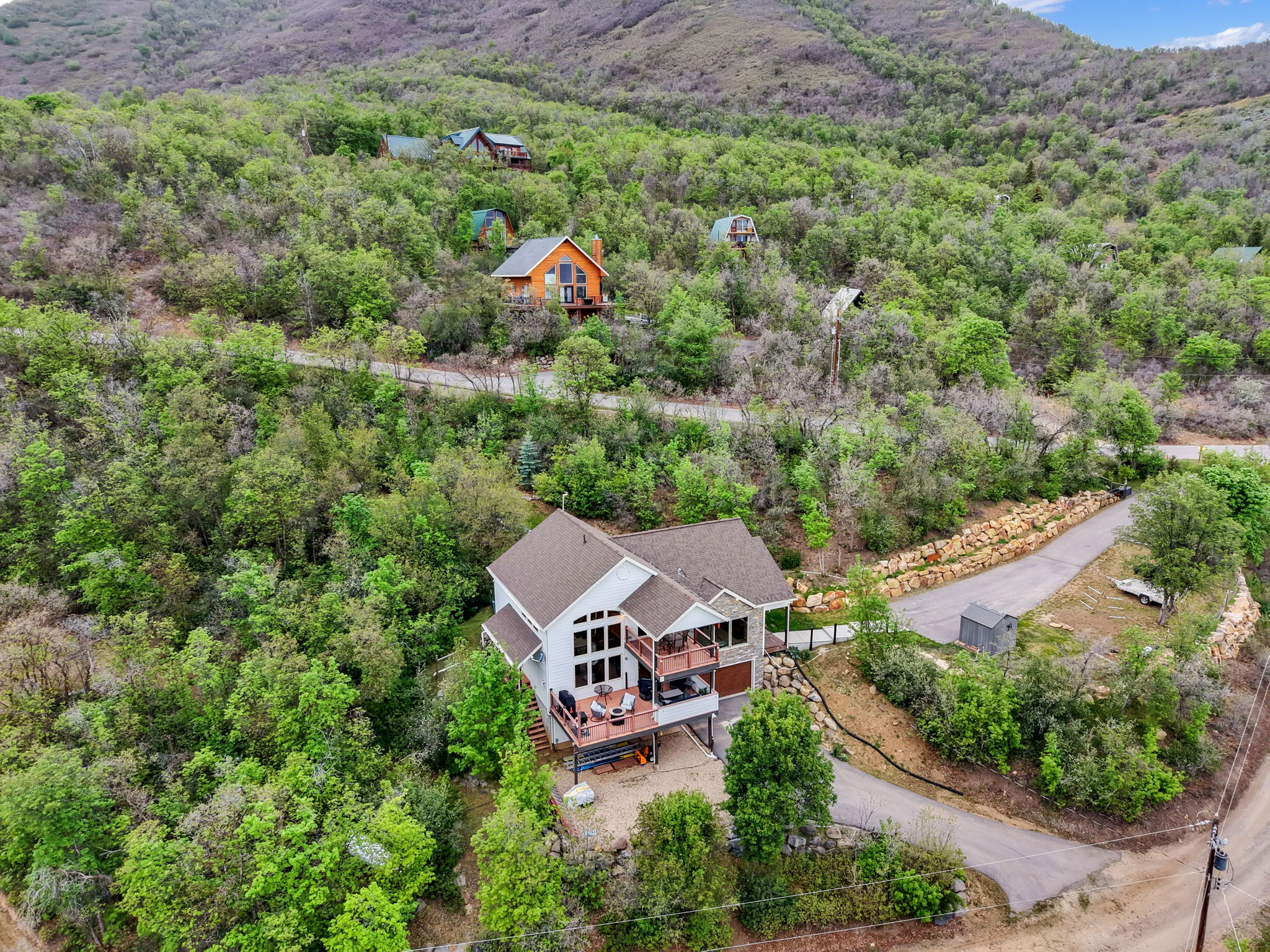 Two-story property nestled into a wooded hillside, featuring a multi-level deck and a stone facade