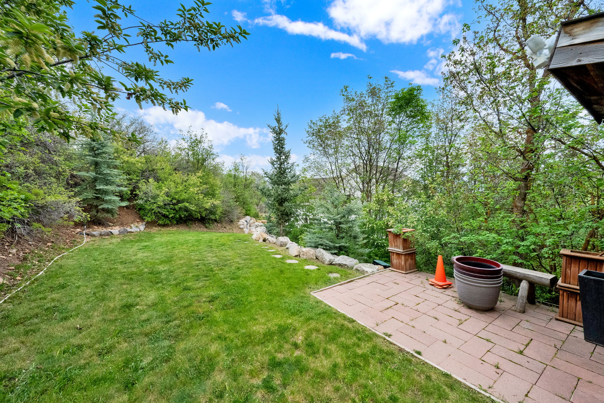 Spacious backyard featuring a manicured lawn, a stone-bordered retaining wall, and a paver patio