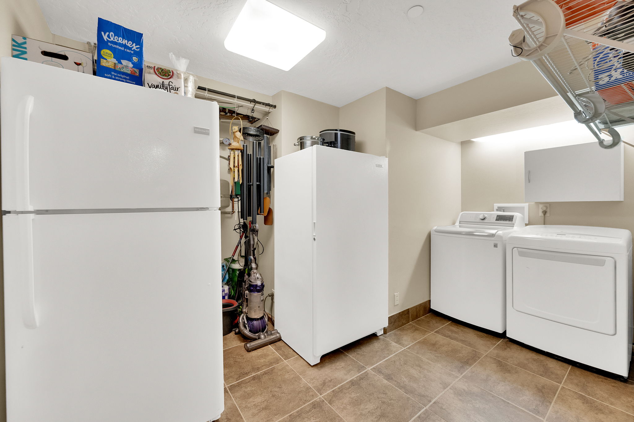 Utility area featuring tile flooring, white wall cabinets, a white refrigerator, a white freezer, and a white washer and dryer set