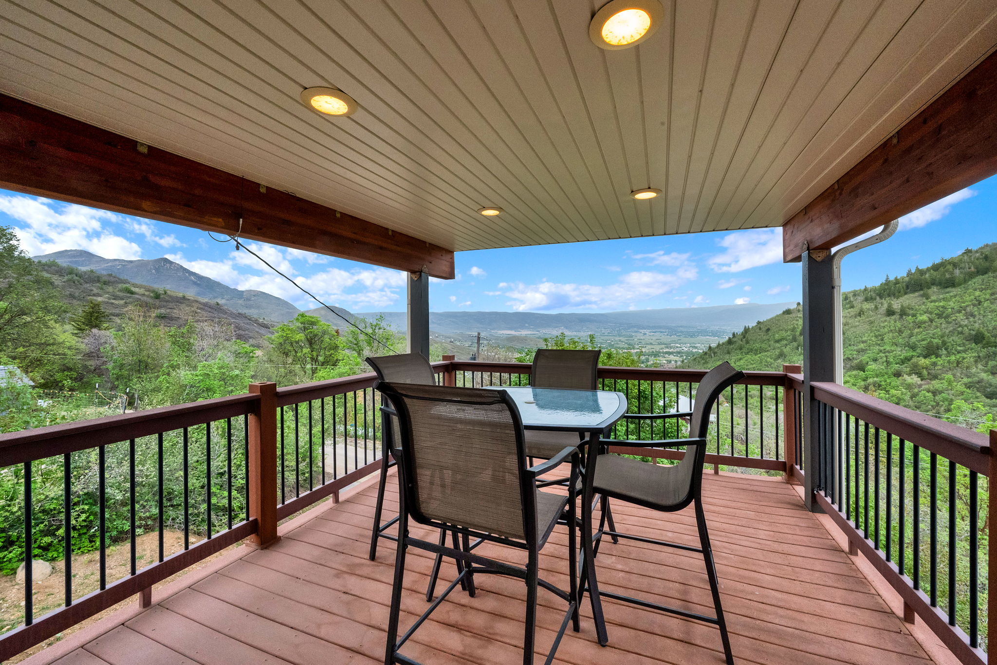 Covered outdoor deck featuring wood-finish flooring, dark wood railings with black balusters, and recessed ceiling lighting