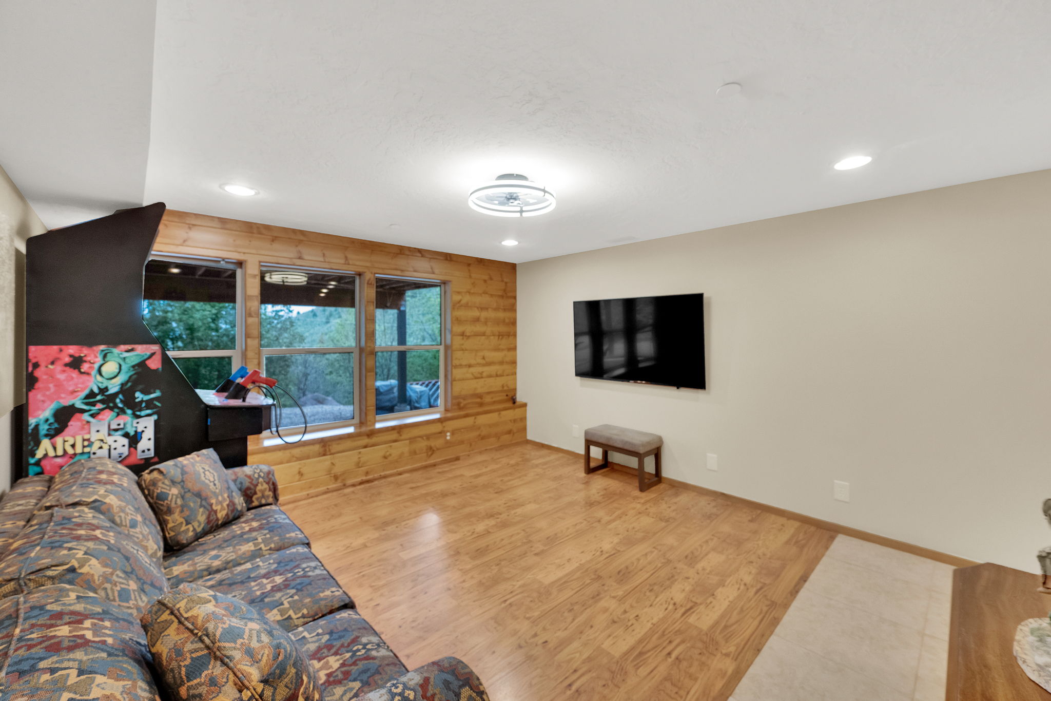 Recreation room featuring three large windows, wood-finish flooring, a wood accent wall, recessed lighting, and a contemporary ceiling fixture