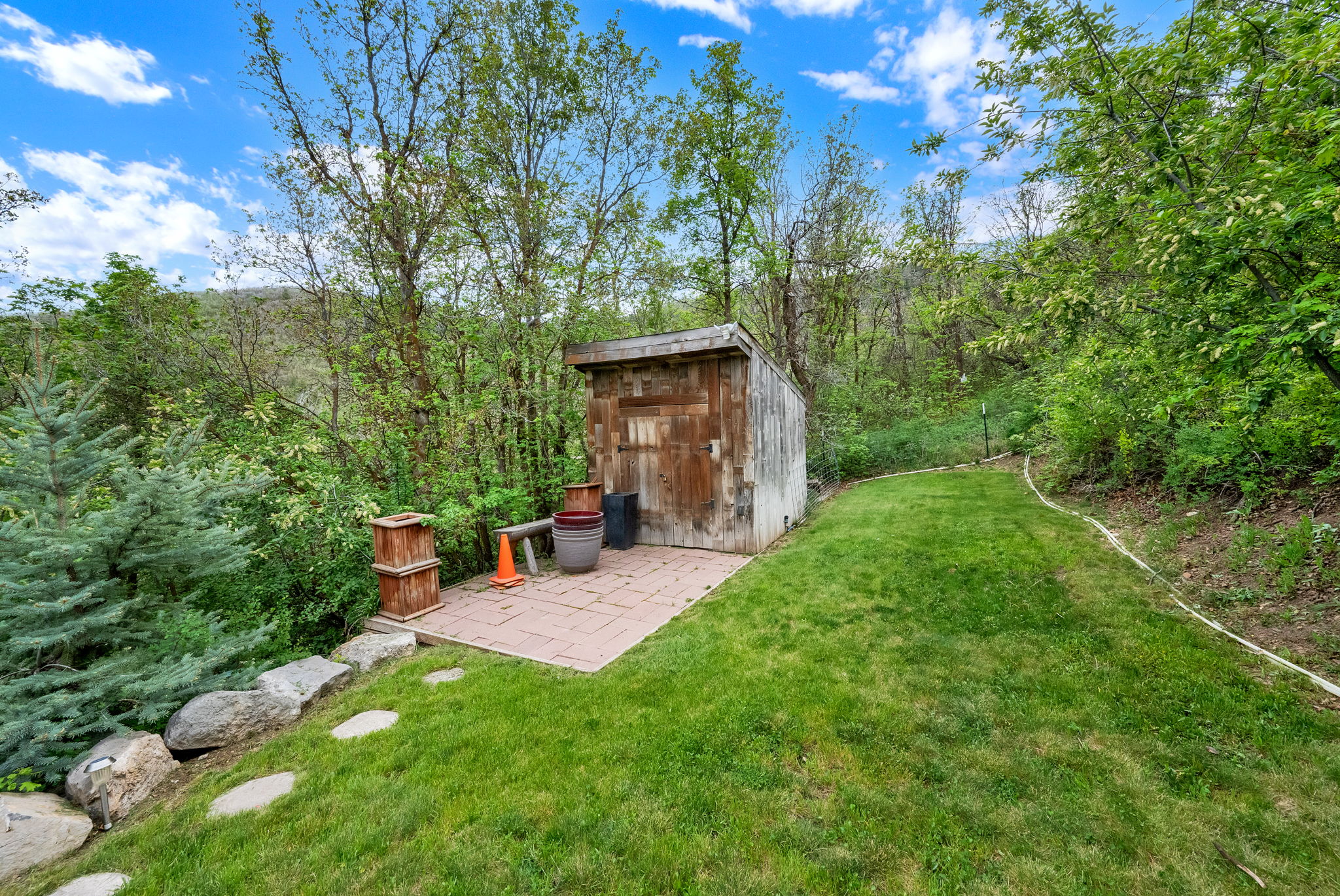 Wood-clad storage shed with a shingle roof situated on a paver patio