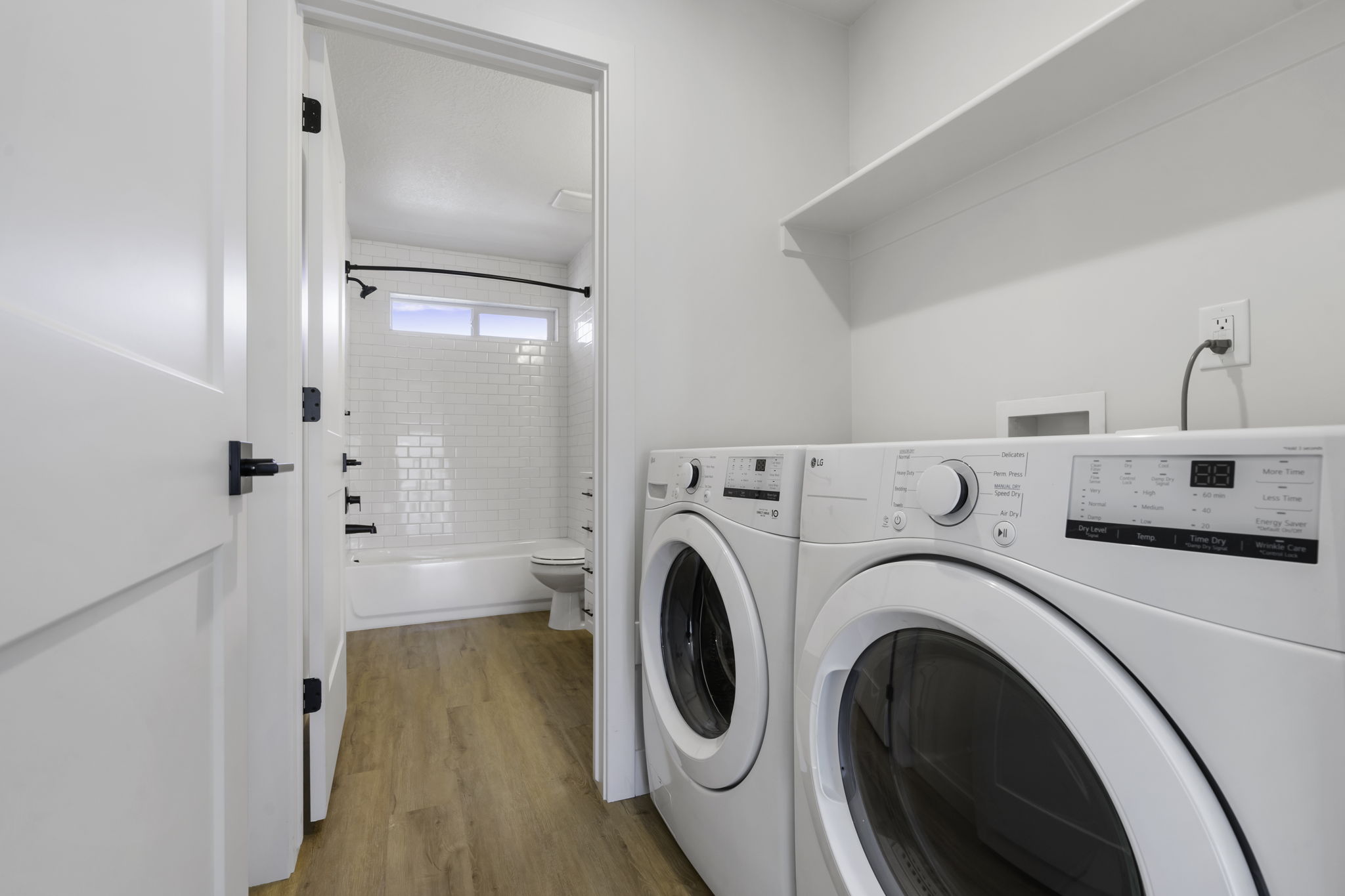 Dedicated laundry area featuring a built-in shelf, wood-finish flooring, and a white interior door with matte black hardware