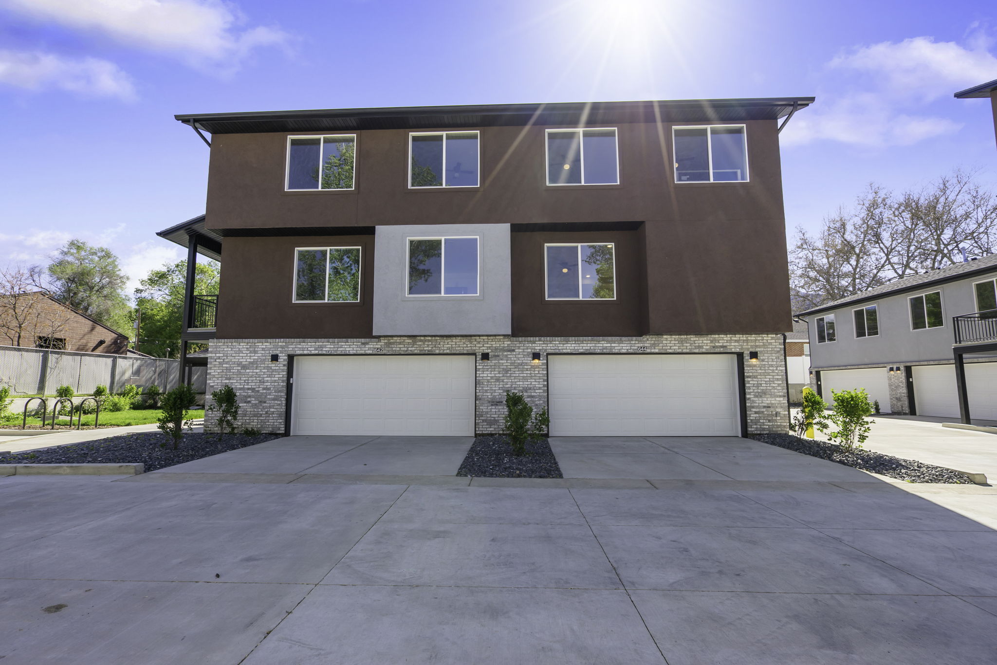Contemporary multi-level exterior featuring a brown stucco finish, stacked stone accent, and multiple large windows