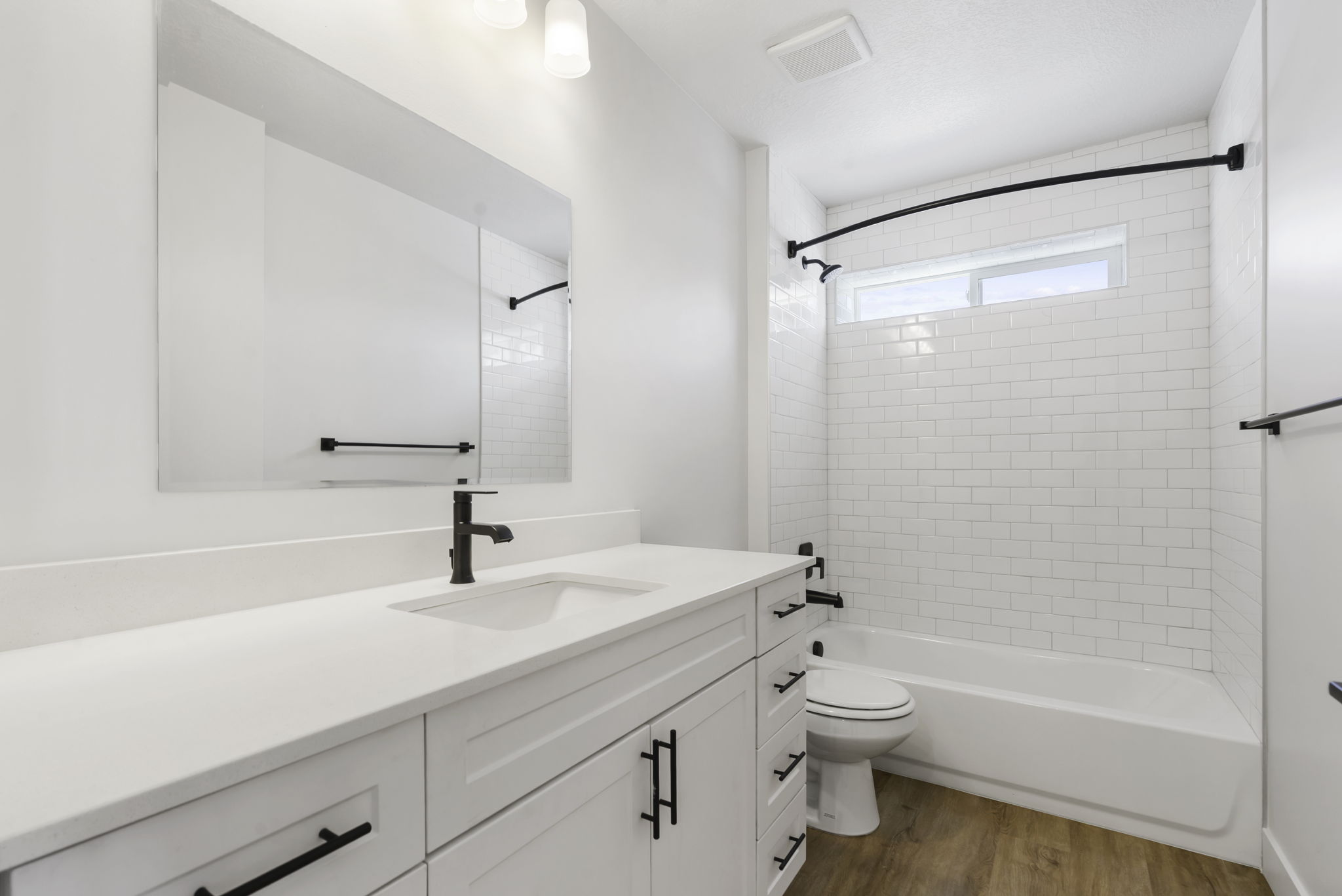 Bathroom featuring a white vanity with an integrated sink and matte black faucet, a large rectangular mirror, and a white subway tile tub surround