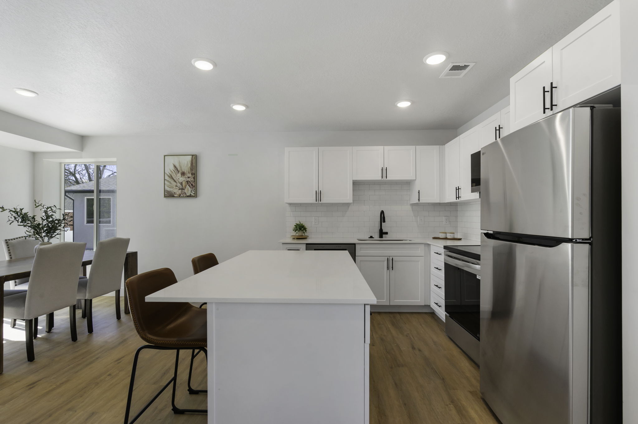 Open-concept kitchen featuring an island with a white countertop, white cabinetry with matte black hardware, stainless steel appliances, and wood-finish flooring