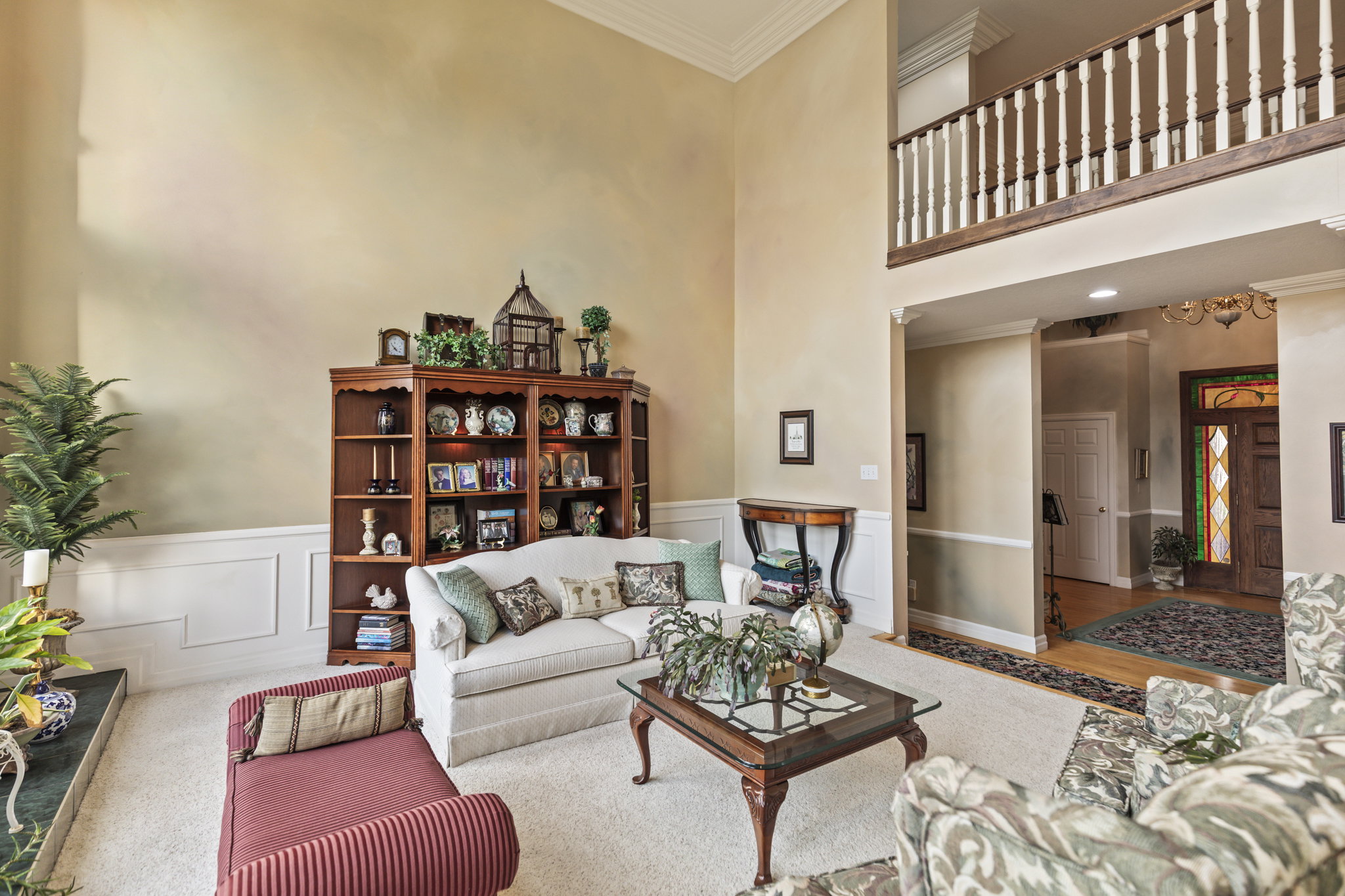 Living room with ornamental molding, a decorative wall, a wainscoted wall, and a high ceiling