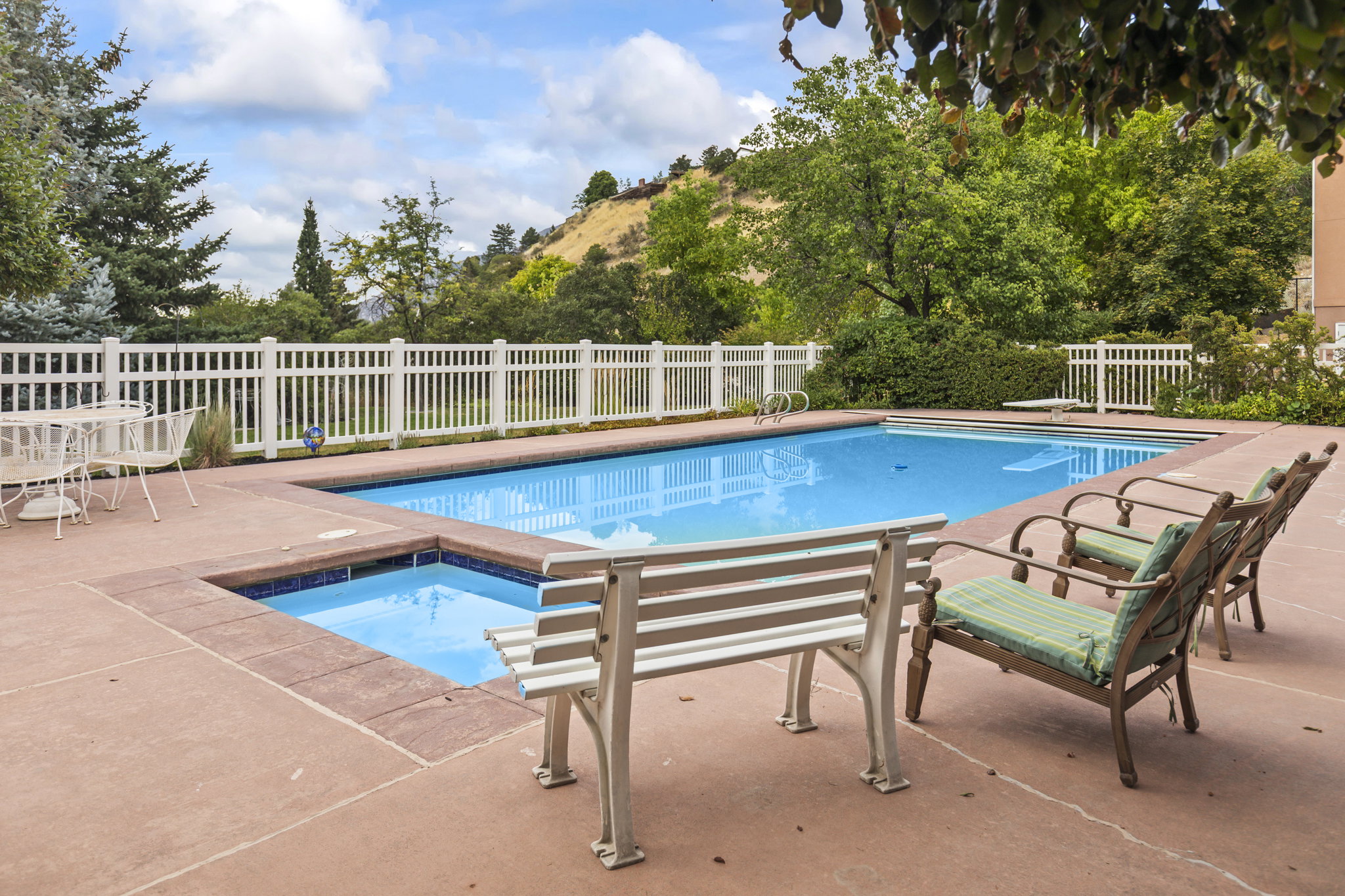 View of pool featuring patio surround, view of wooded area, and an in-ground hot tub