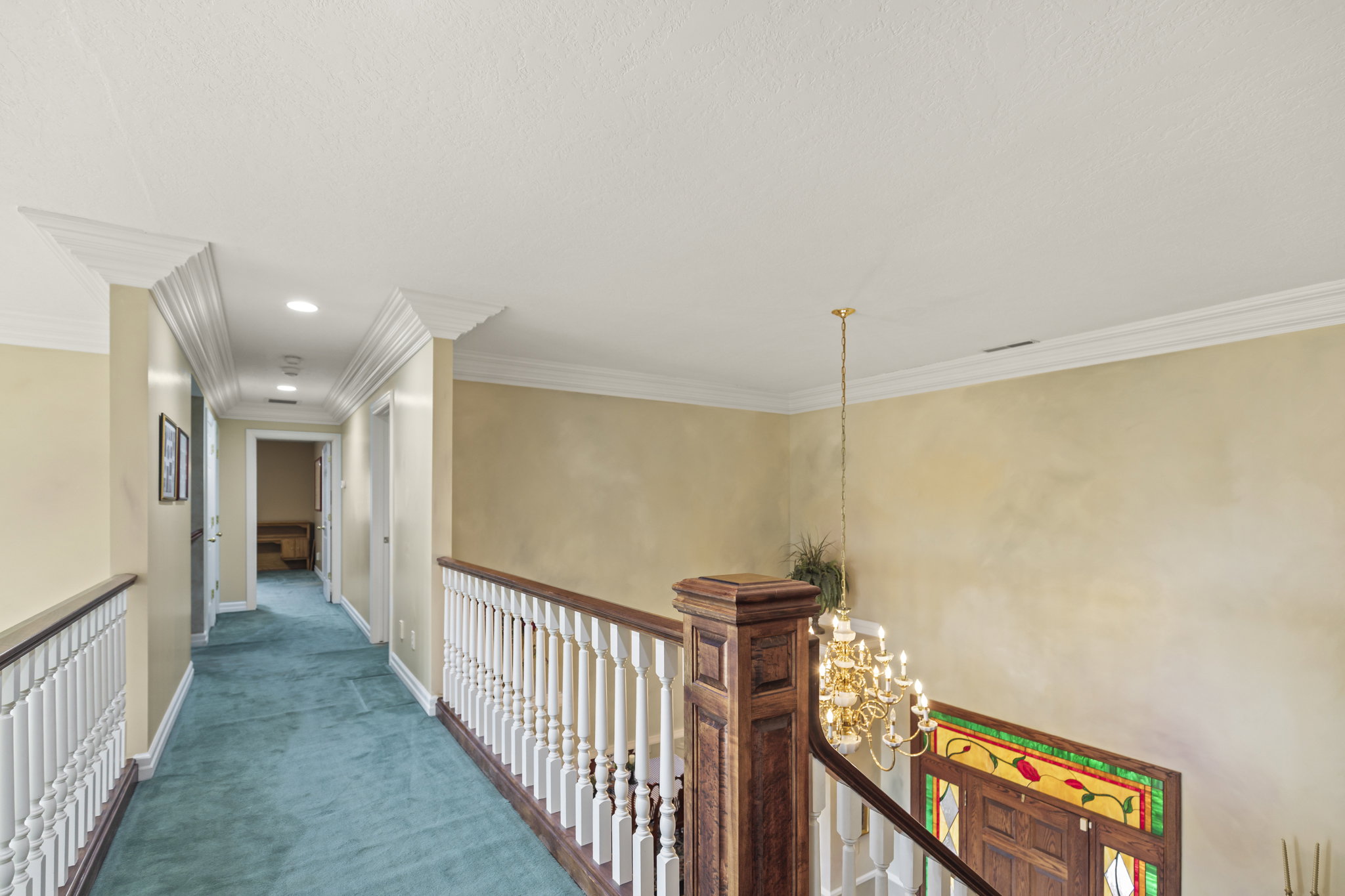 Corridor with suspended lighting, carpet flooring, ornamental molding, and an upstairs landing