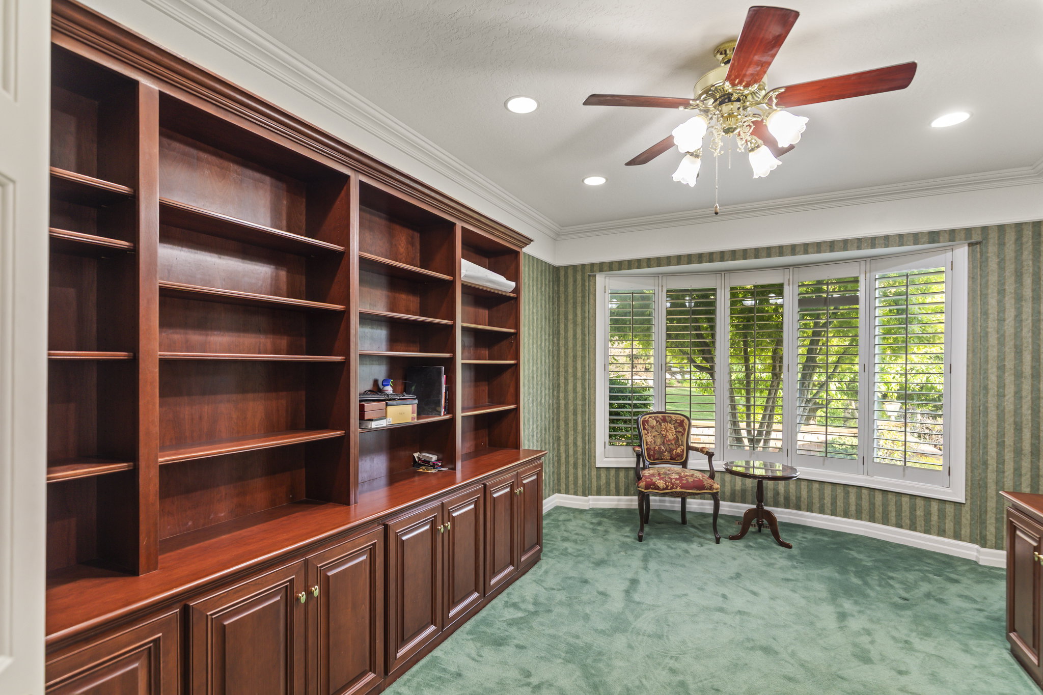 Living area with wallpapered walls, dark colored carpet, a ceiling fan, and crown molding