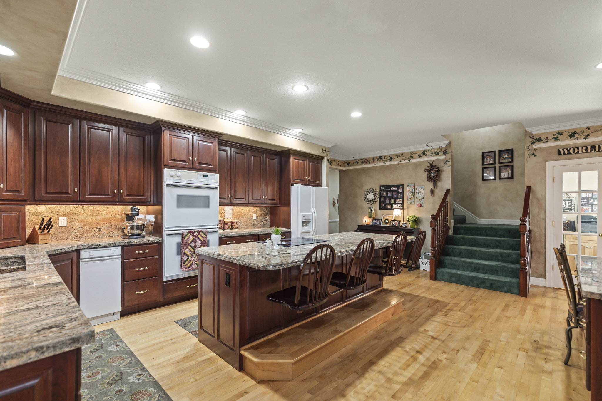Kitchen with ornamental molding, a kitchen island, dark wood finish cabinetry, white appliances, and light stone countertops