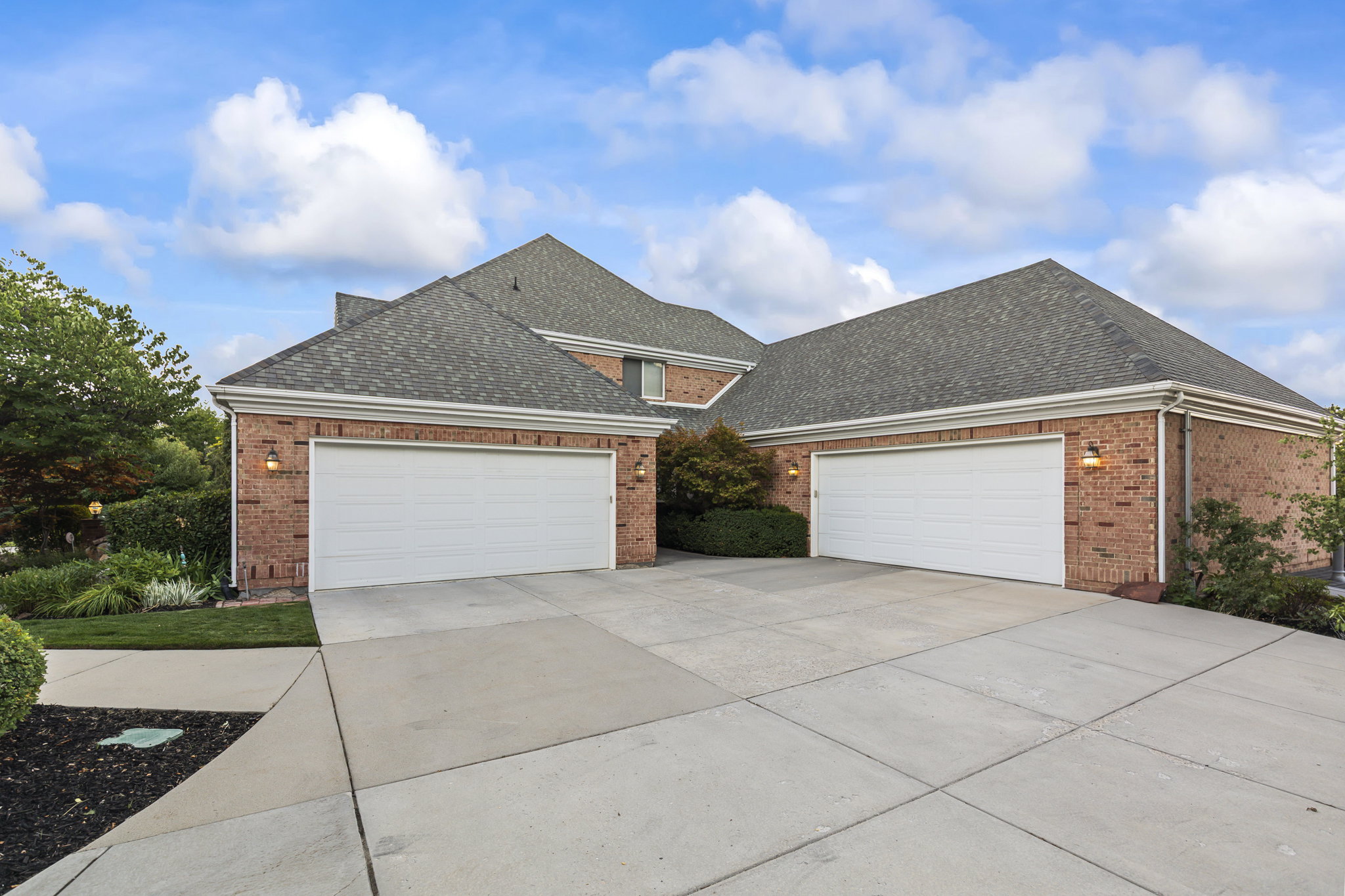 Traditional-style home featuring a shingled roof, brick siding, a garage, and driveway