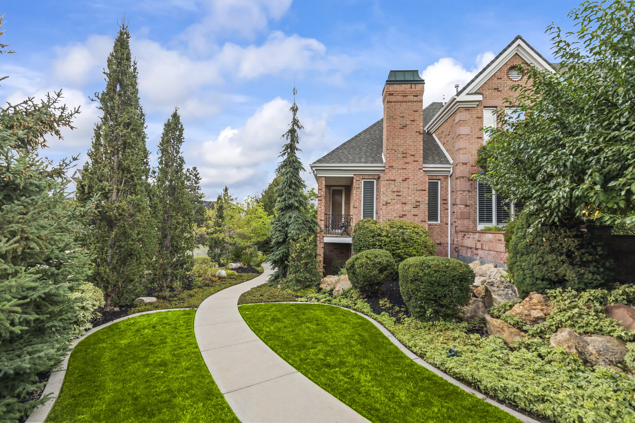 View of front of home with brick siding, a front lawn, a balcony, a chimney, and roof with shingles