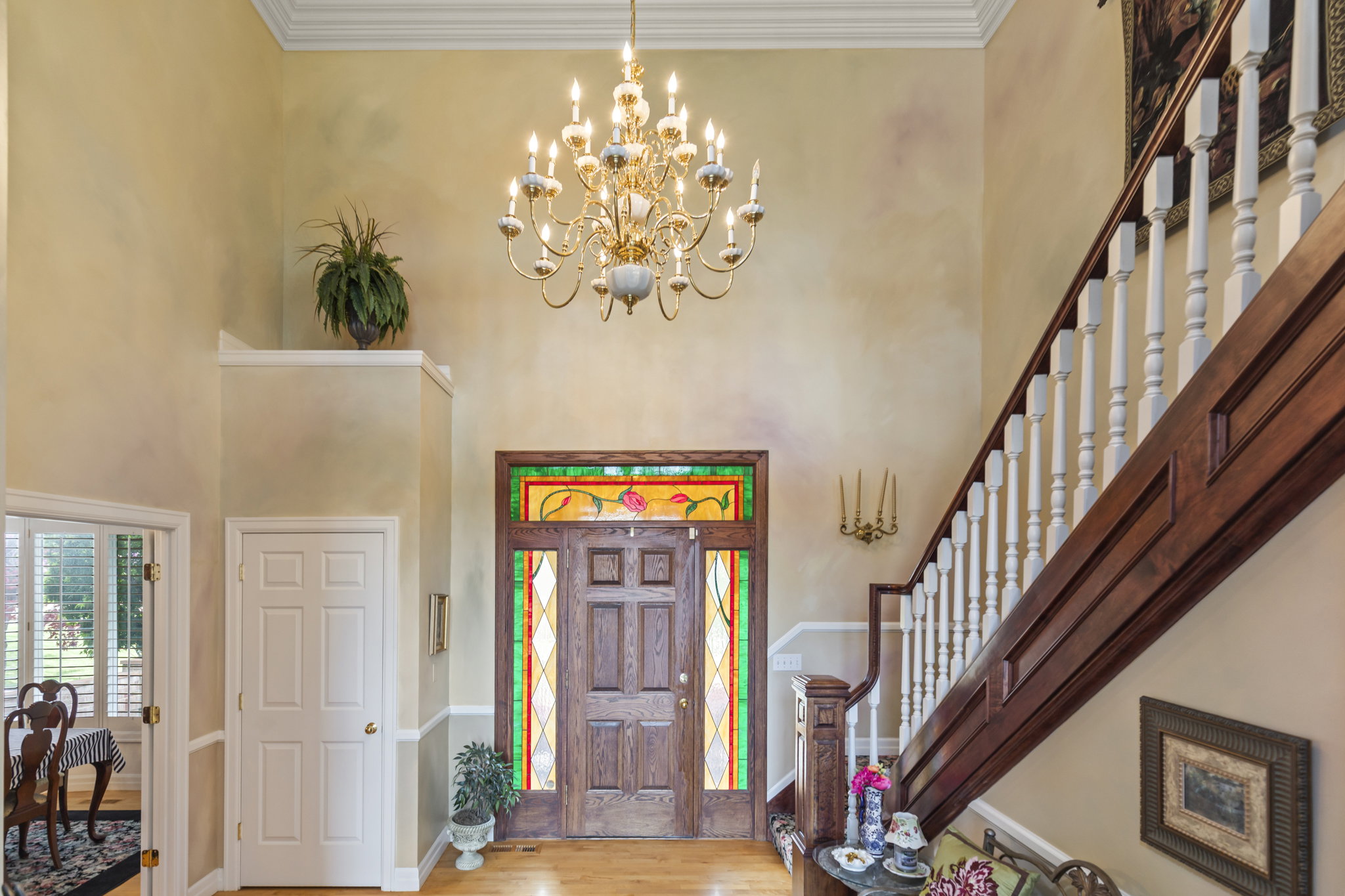 Entryway with hanging lights, a high ceiling, crown molding, and light wood-style floors