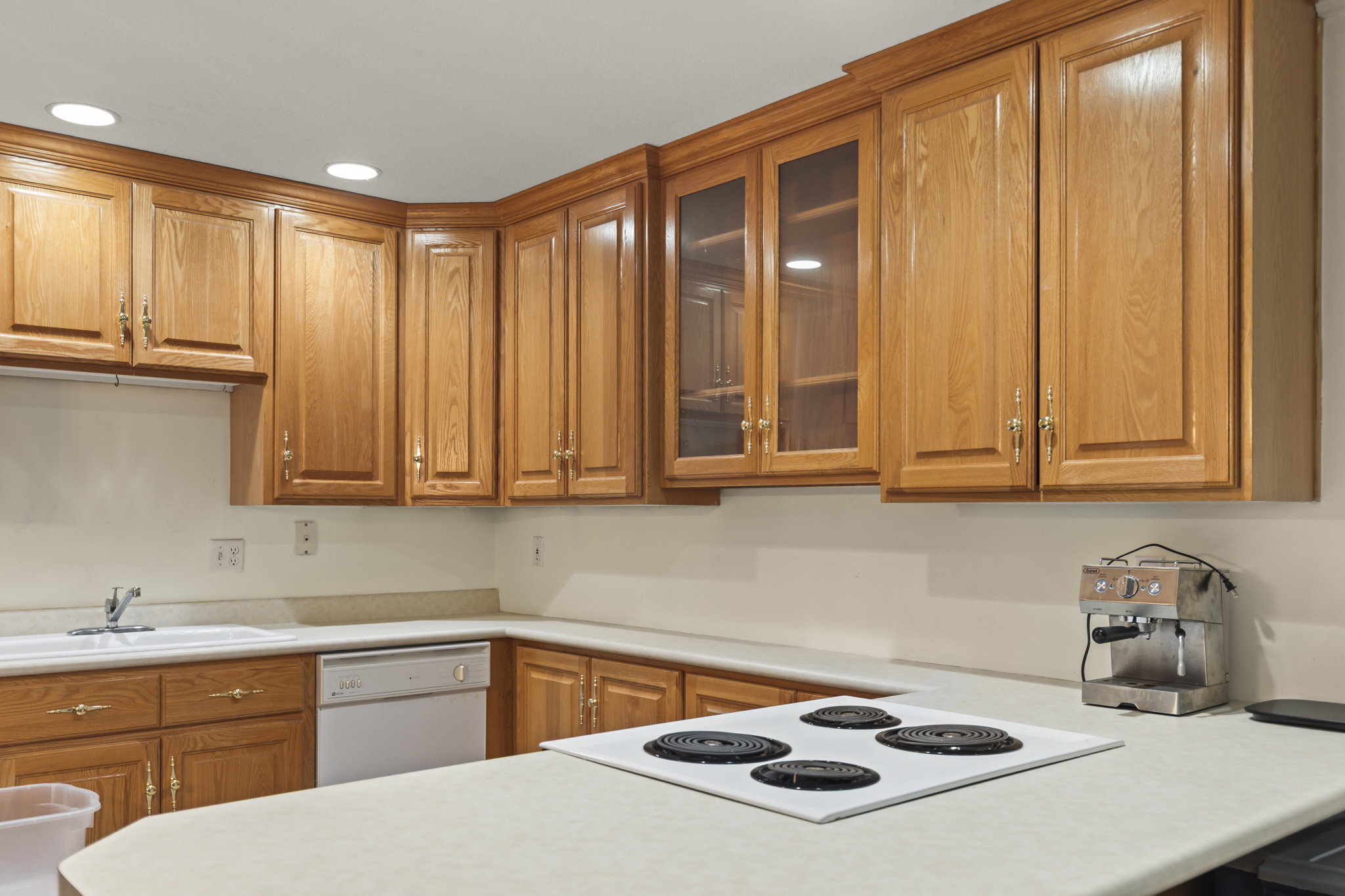 Kitchen featuring glass fronted cabinets, light countertops, wood finish cabinetry, recessed lighting, and dishwasher