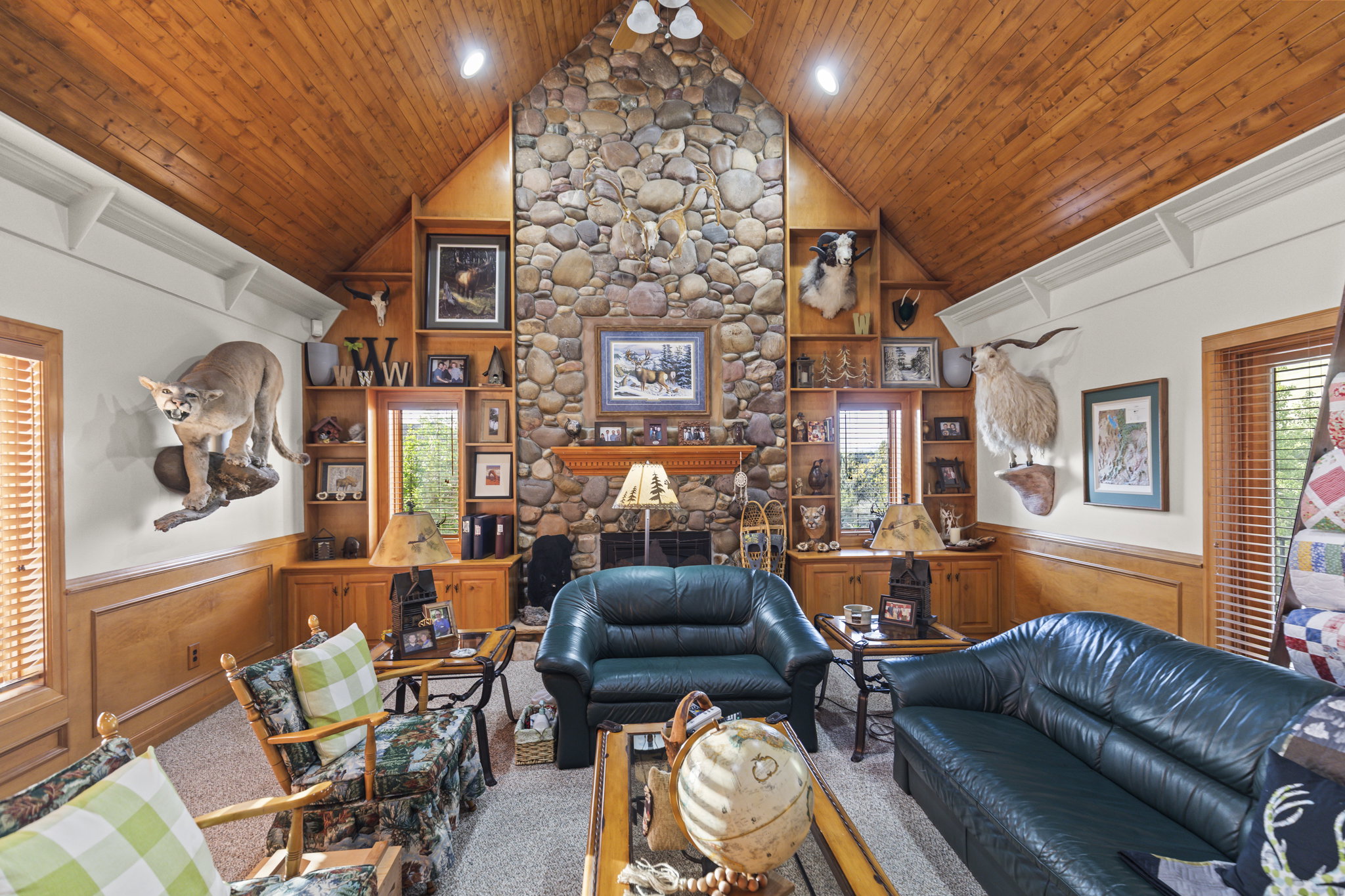 Living area with a wainscoted wall, plenty of natural light, a stone fireplace, a decorative wall, and ceiling fan
