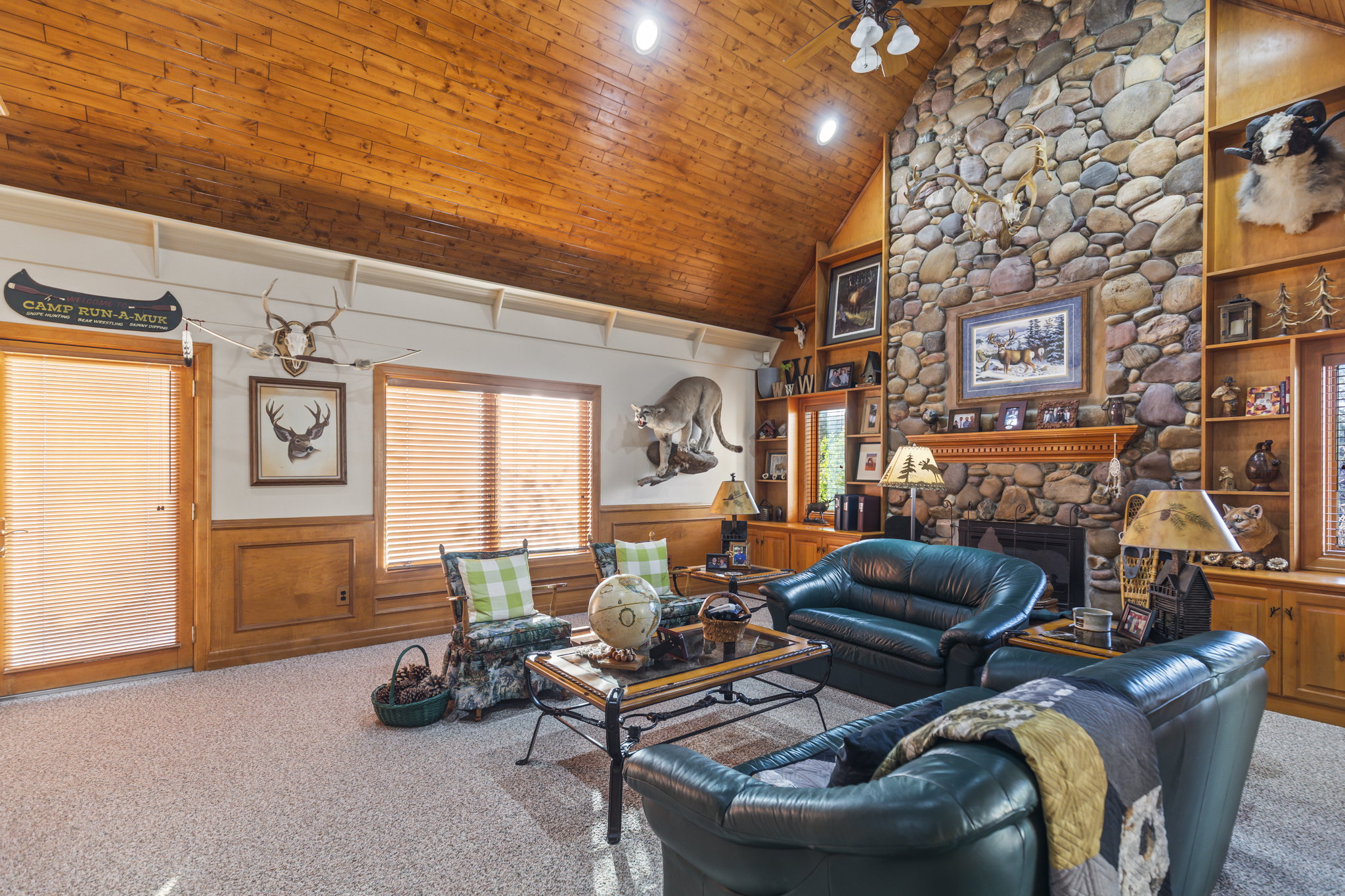 Carpeted living room with a wainscoted wall, a vaulted wooden ceiling, a decorative wall, a fireplace, and a ceiling fan