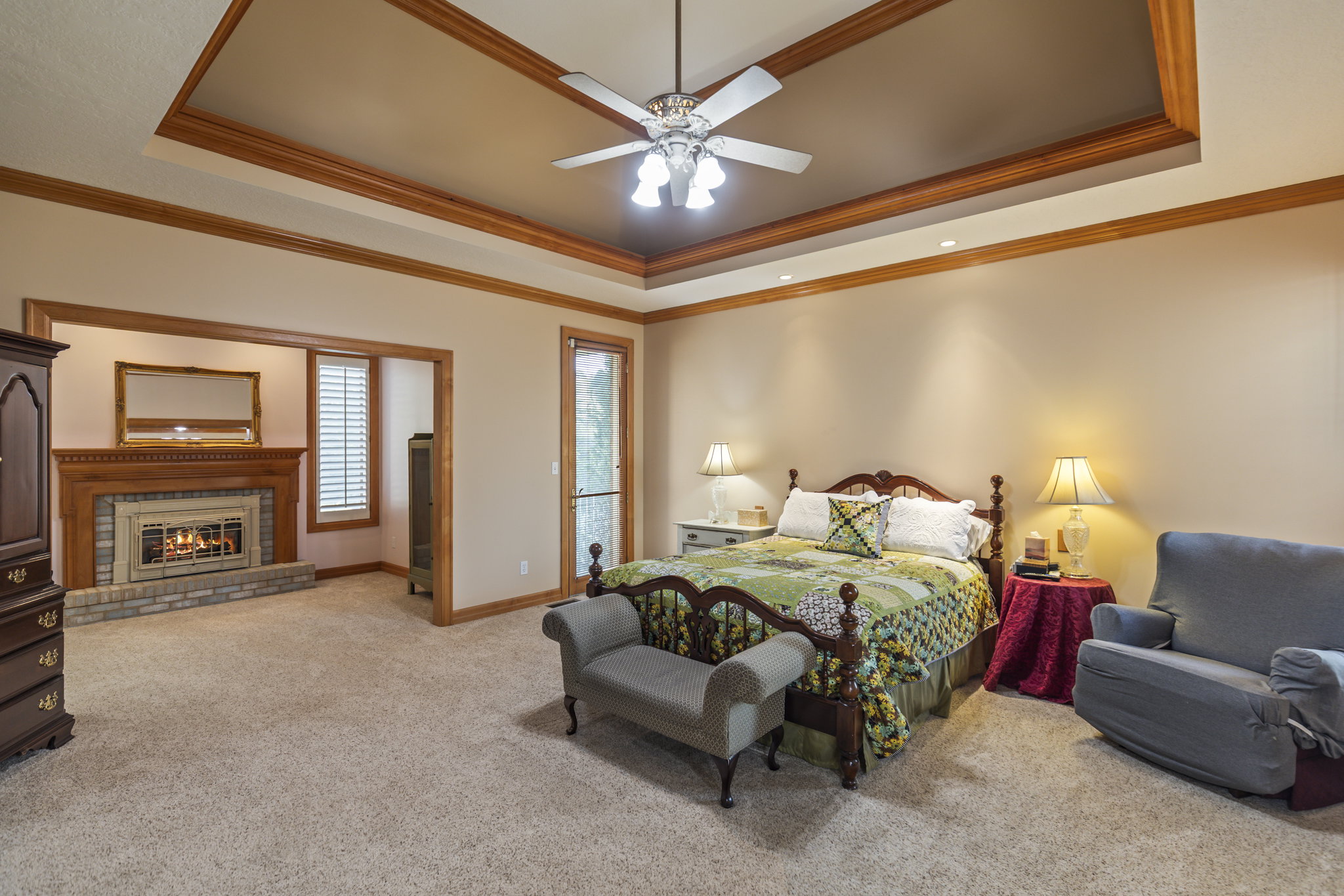 Bedroom with a fireplace, light colored carpet, a raised ceiling, ceiling fan, and ornamental molding