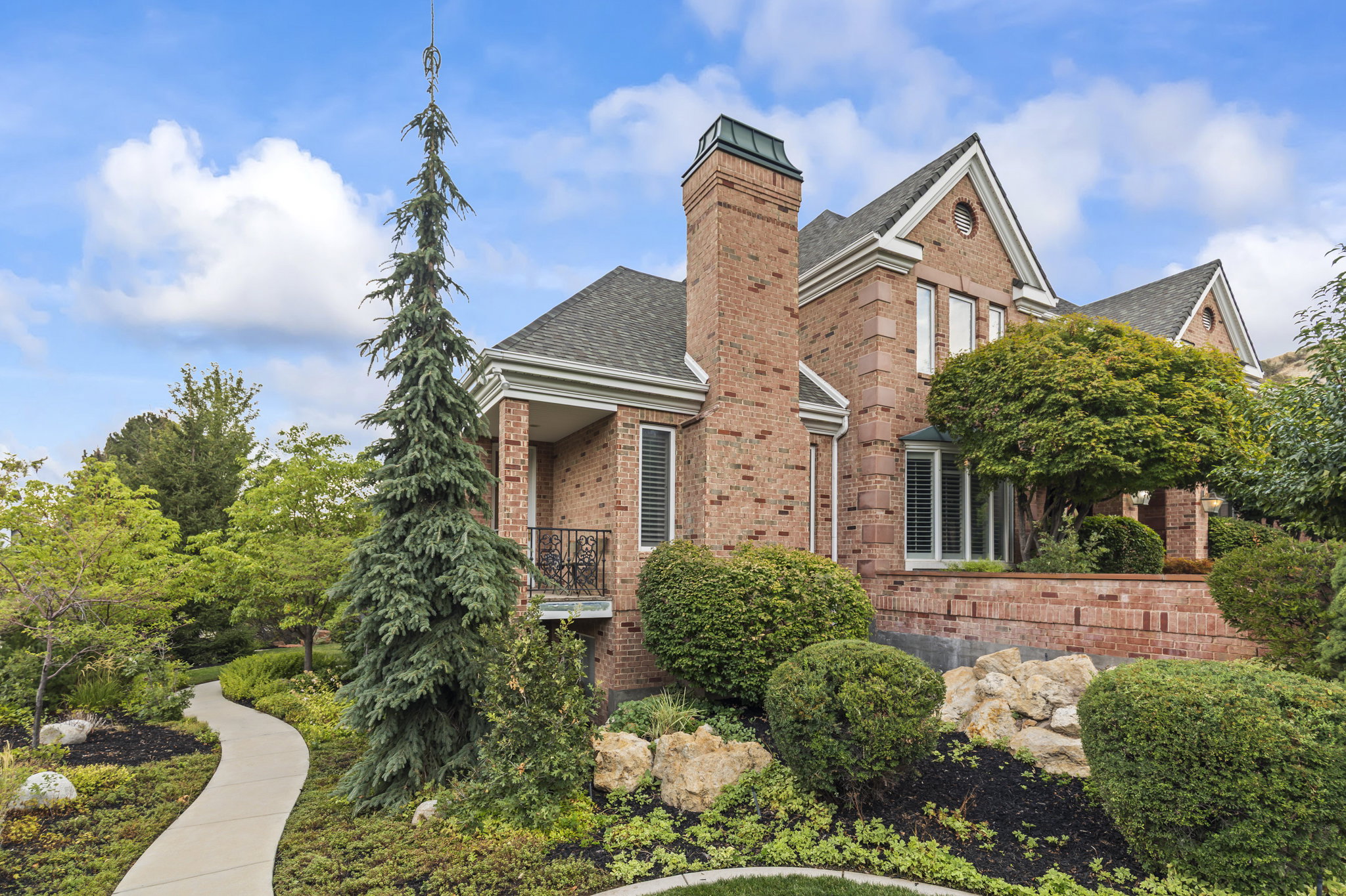 View of front of house featuring brick siding, a shingled roof, a balcony, and a chimney
