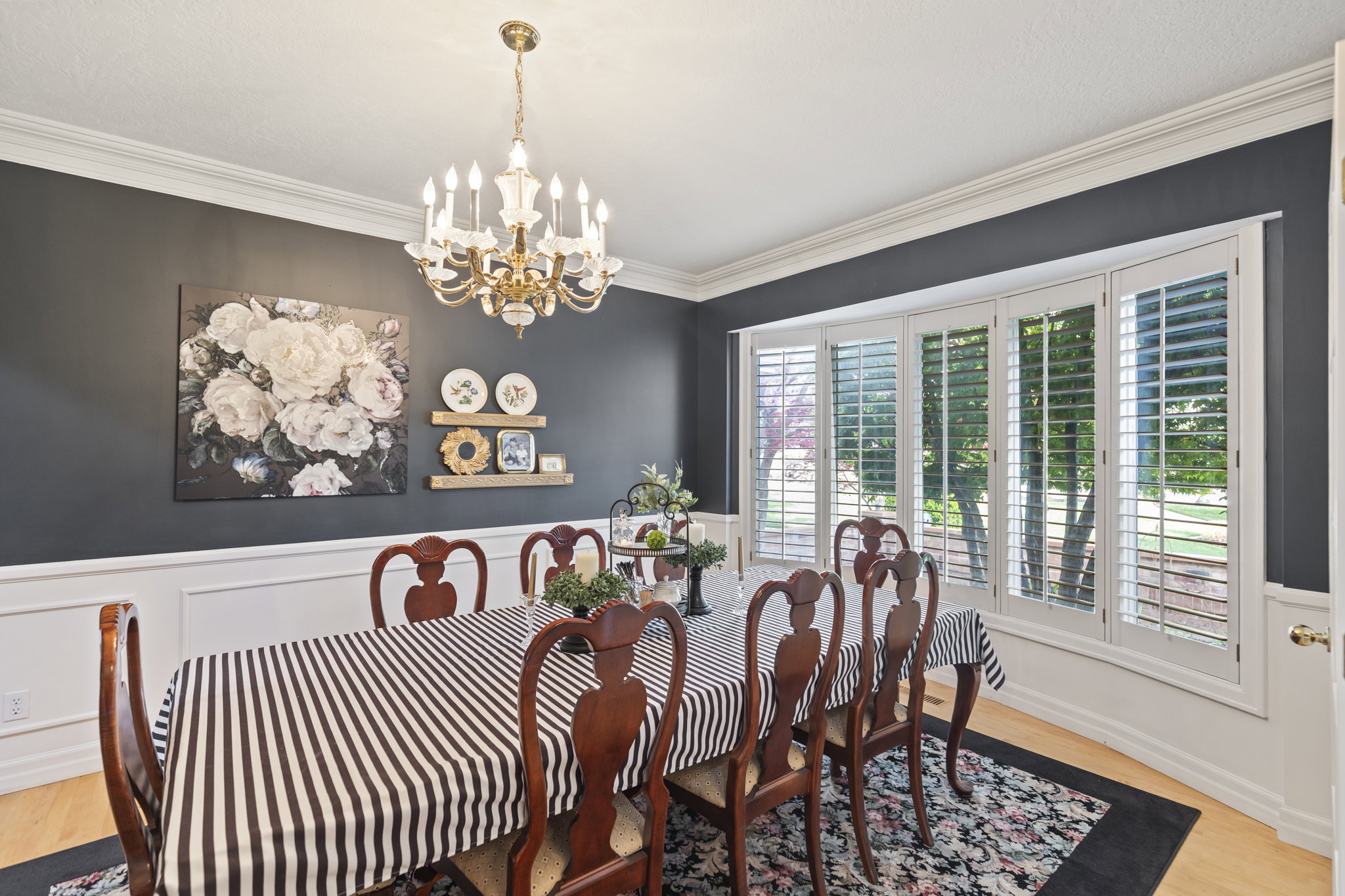 Dining space with wood finished floors, a chandelier, crown molding, wainscoting, and a decorative wall