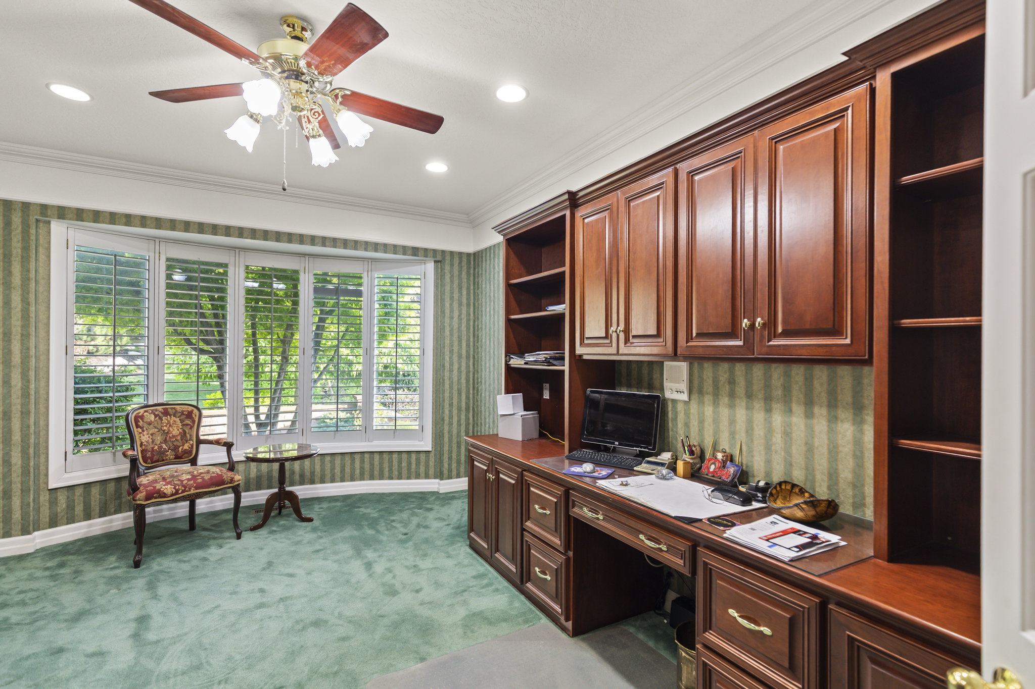 Office space featuring wallpapered walls, built in study area, light carpet, ceiling fan, and ornamental molding