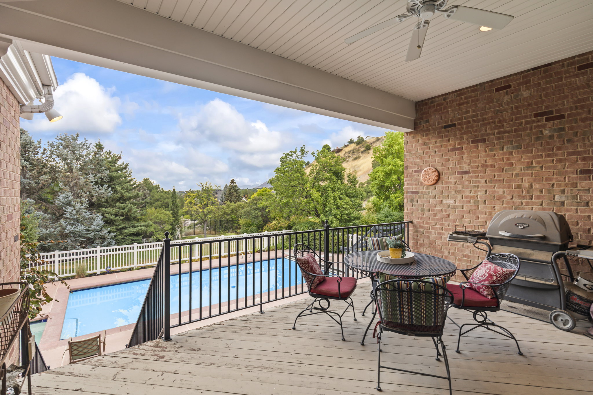 Wooden deck with ceiling fan, outdoor dining space, and view of scattered trees