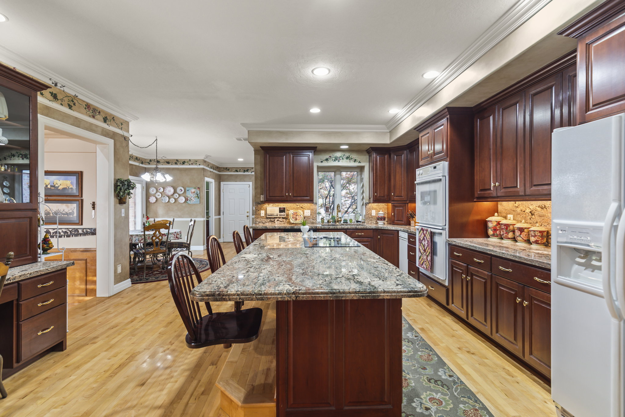 Kitchen featuring a breakfast bar, white appliances, light wood-style floors, light stone counters, and crown molding