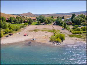 Aerial photo of expansive waterfront property featuring a sandy beach, clear blue water, and a mountainous backdrop