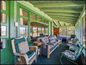 Expansive screened porch featuring a green painted exposed beam ceiling, a carpeted floor, and large screened panels
