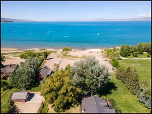 Aerial perspective showcasing expansive waterfront access, sandy shoreline, mature trees, and a manicured green space.  Taken from the air from behind the cabin towards the north.