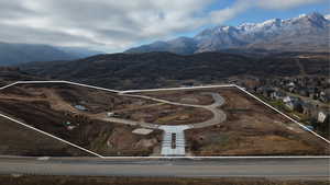 Expansive land parcel featuring partial road infrastructure, mountain backdrop, and a neighboring residential community