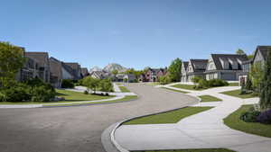 Curving streetscape featuring diverse architectural styles, landscaped front yards, concrete sidewalks, and a mountainous backdrop