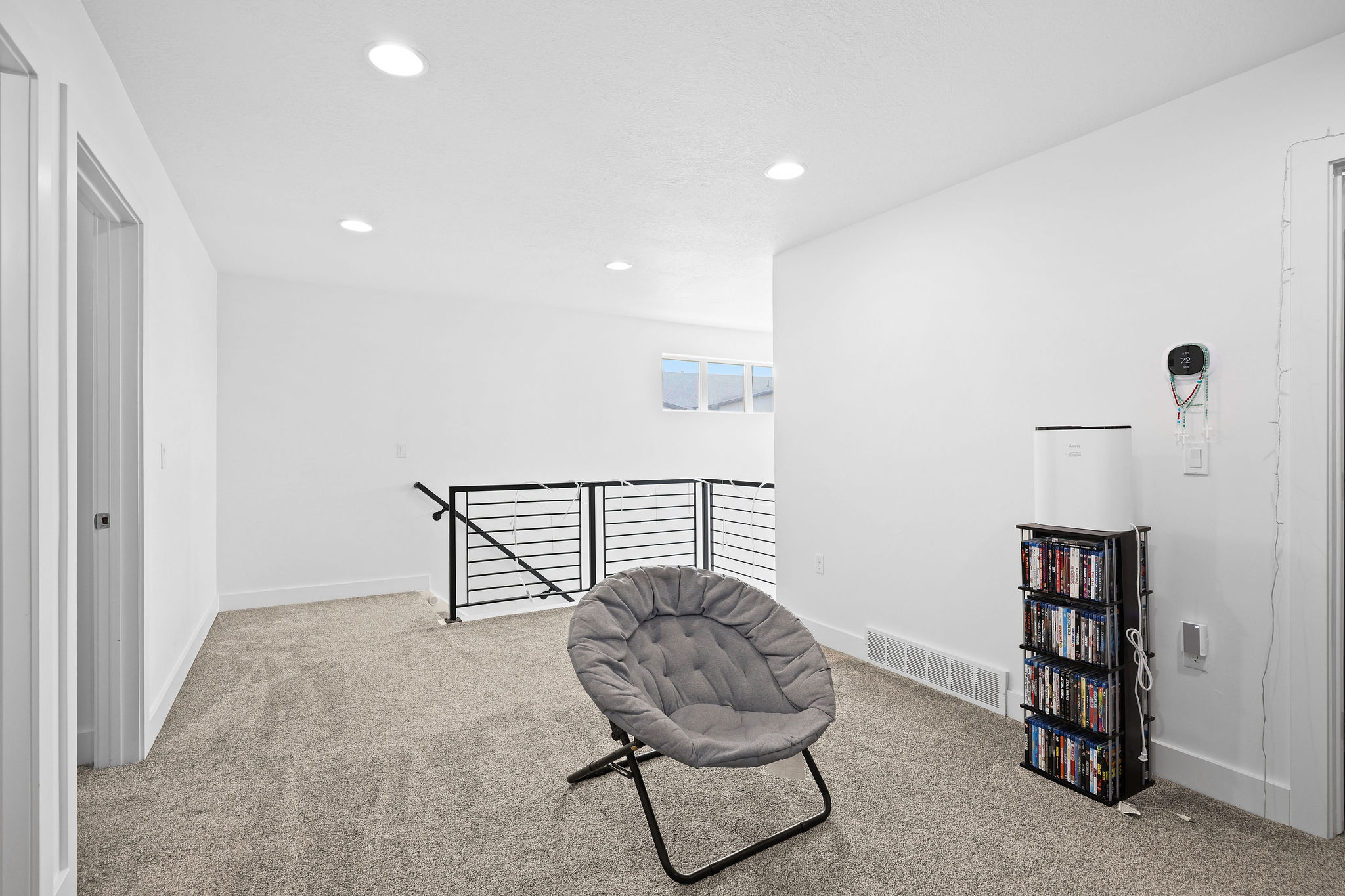 Expansive carpeted loft area featuring a modern black metal railing, a window providing natural light, recessed ceiling lighting, and crisp white walls