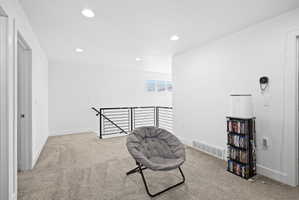 Expansive carpeted loft area featuring a modern black metal railing, a window providing natural light, recessed ceiling lighting, and crisp white walls
