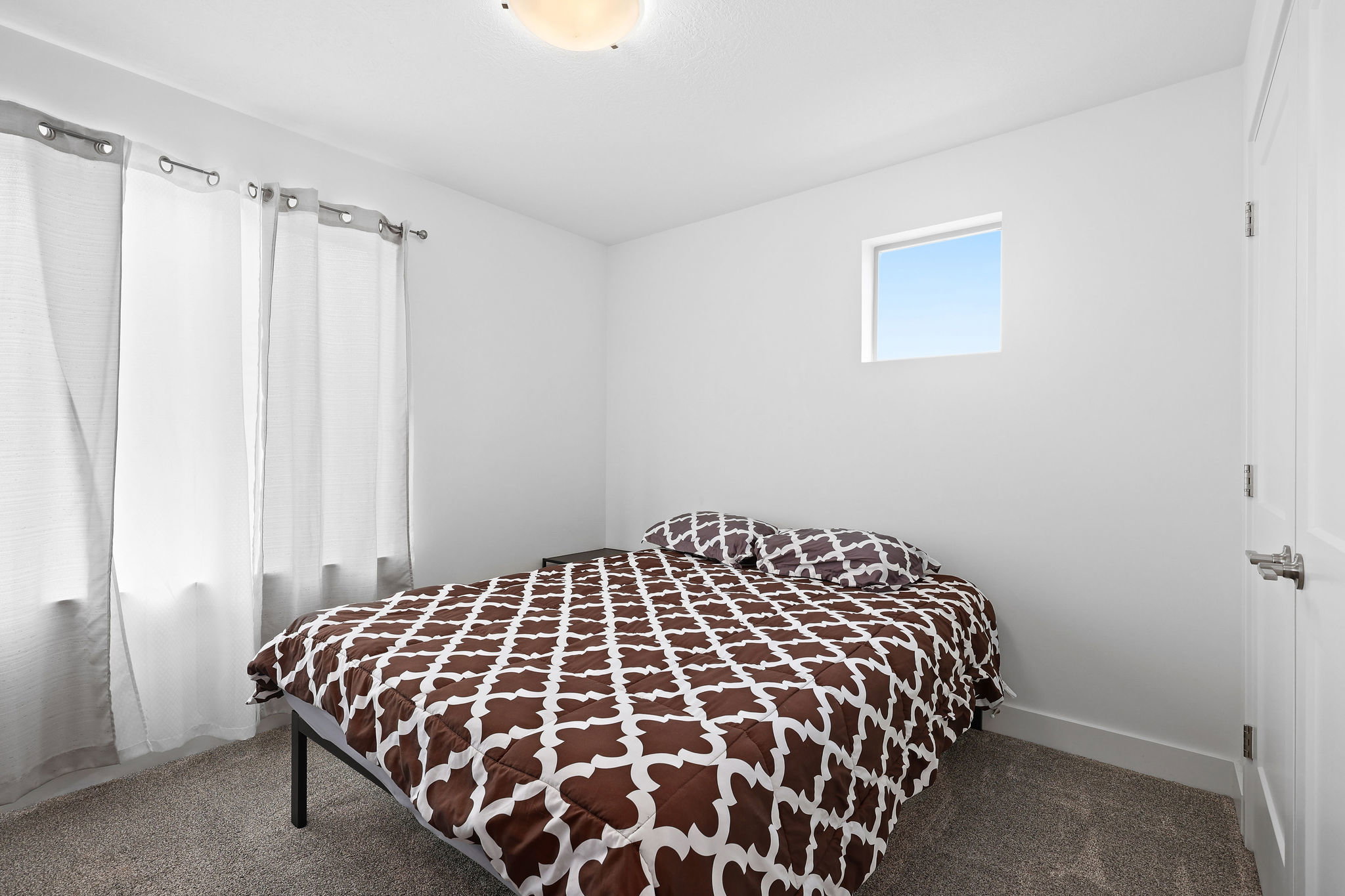 Bright bedroom featuring a flush-mount ceiling light, white walls, and soft grey carpeting