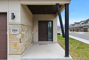 Covered entryway featuring a stone veneer accent wall, contemporary exterior lighting, a dark-stained solid front door with a sidelight, and a concrete porch with a dark-finished support beam