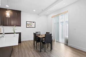 Open-concept dining area featuring wood-finish flooring, a contemporary pendant light fixture, a sliding glass door with vertical blinds, and recessed lighting
