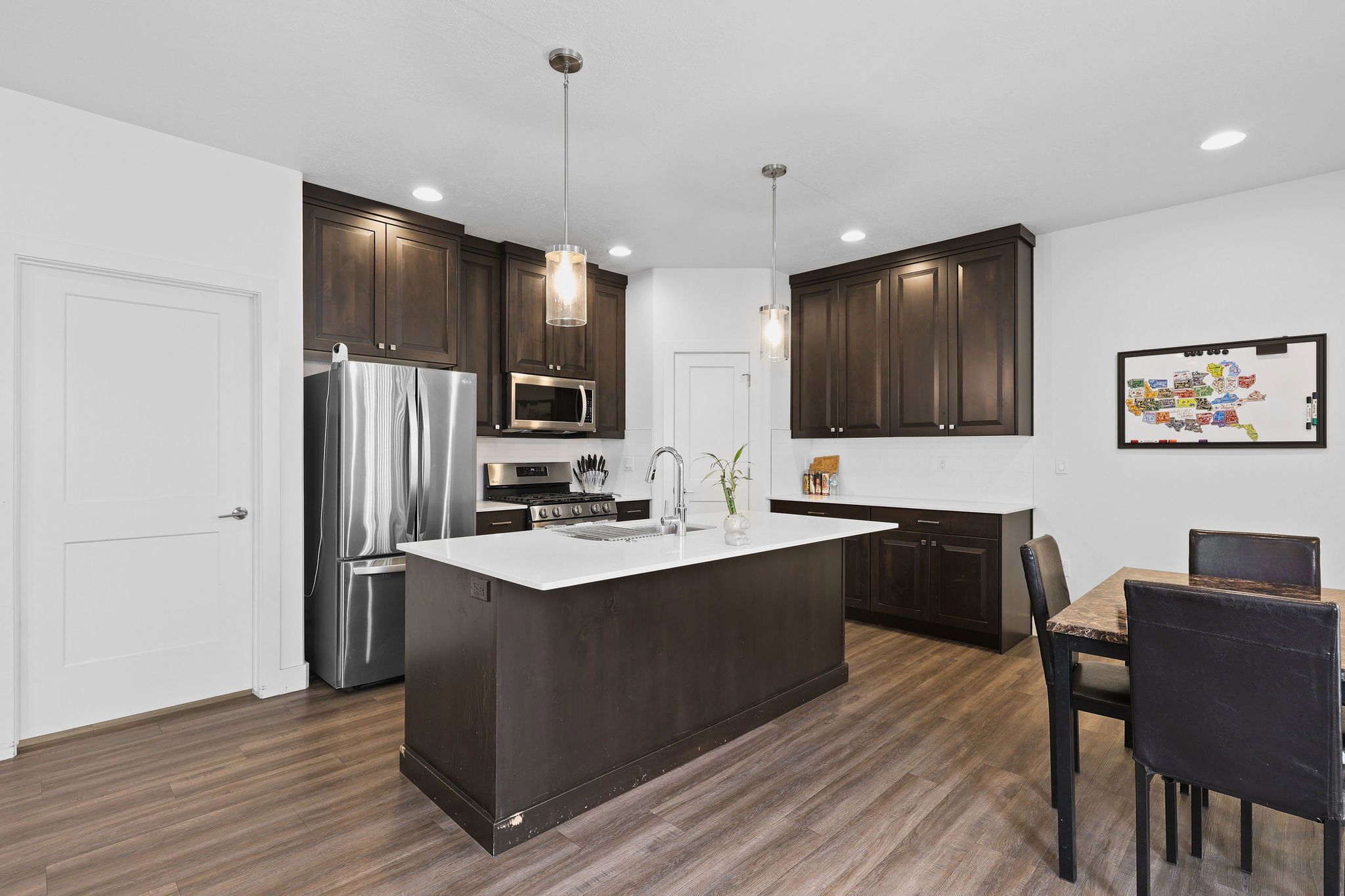 Open-concept kitchen featuring dark wood cabinetry, stainless steel appliances, a center island with white countertop, and wood-finish flooring
