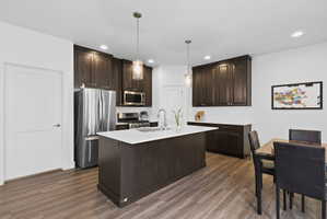 Open-concept kitchen featuring dark wood cabinetry, stainless steel appliances, a center island with white countertop, and wood-finish flooring
