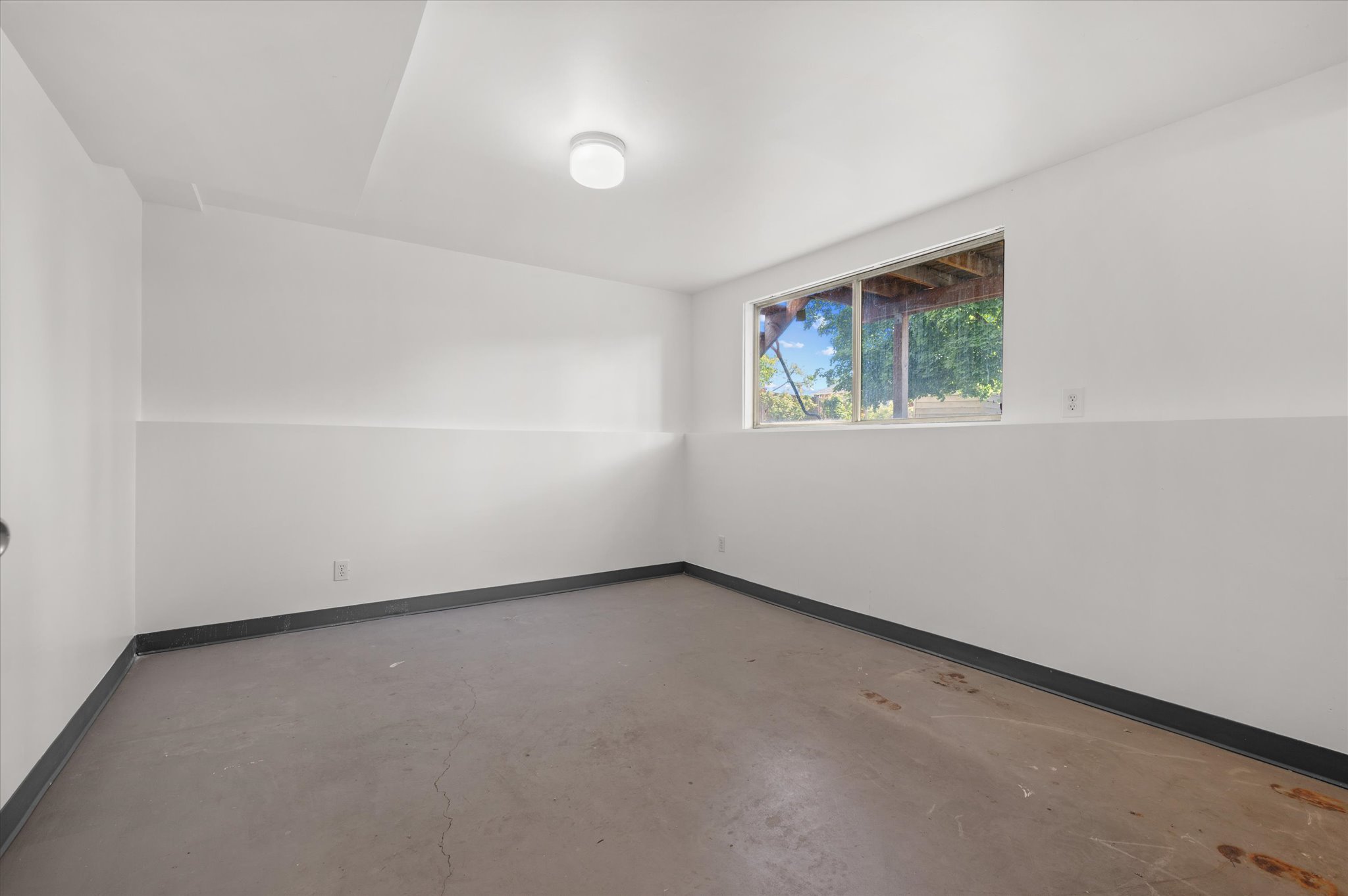 Spacious room with concrete flooring, white painted walls, and a large window
